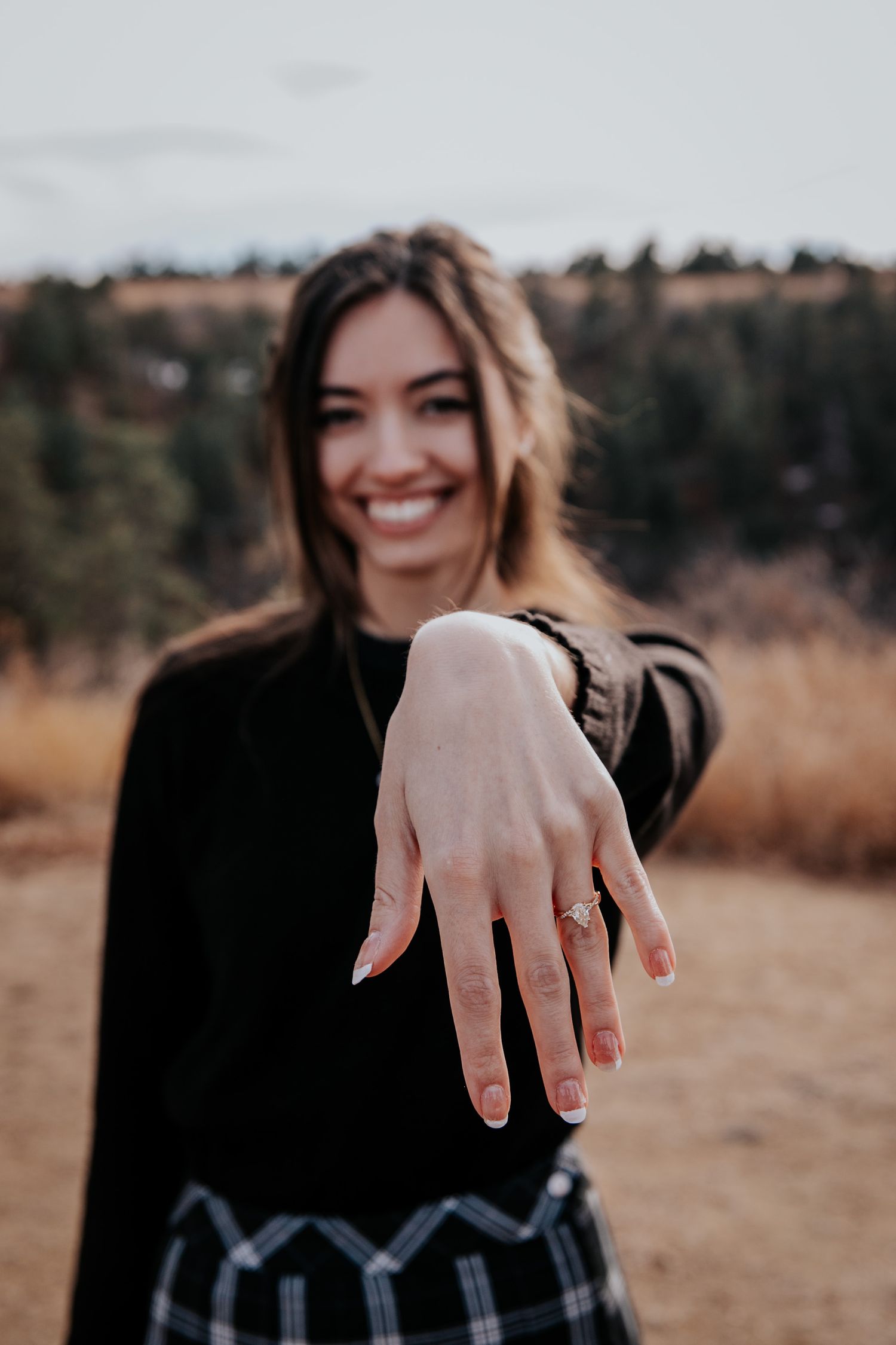 Person showing off engagement ring with mountains and autumn landscape in background.