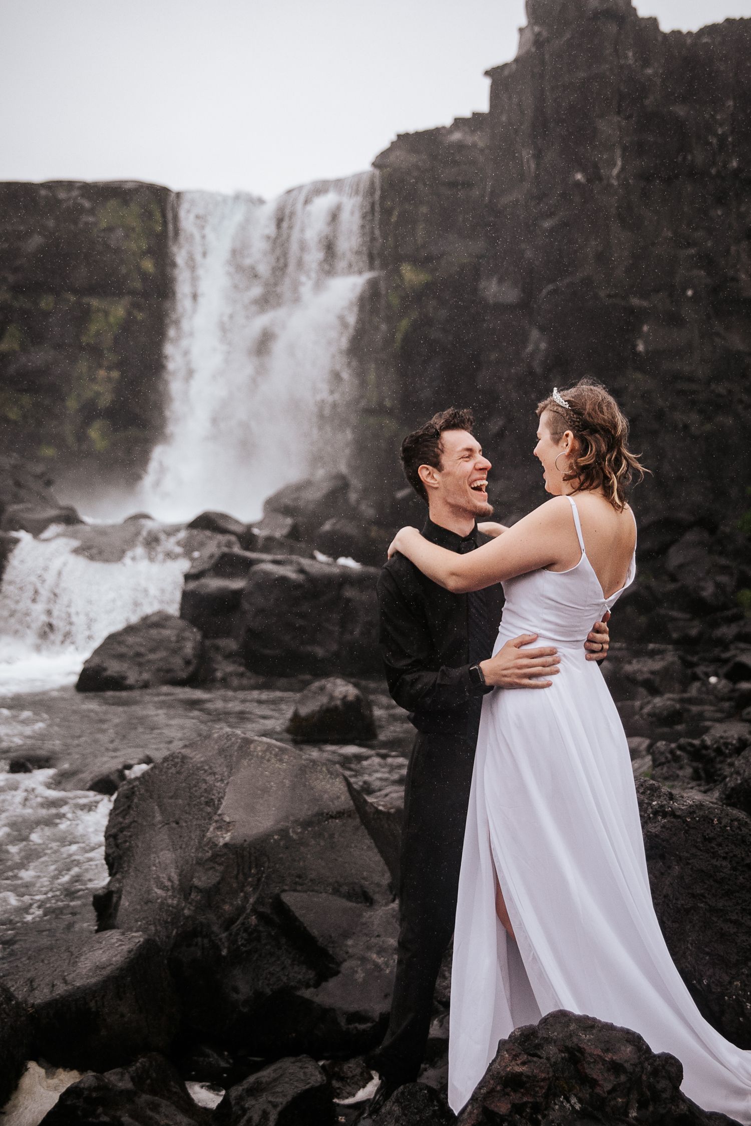 A joyful embrace captured on rocky terrain with a powerful waterfall cascading in the background.