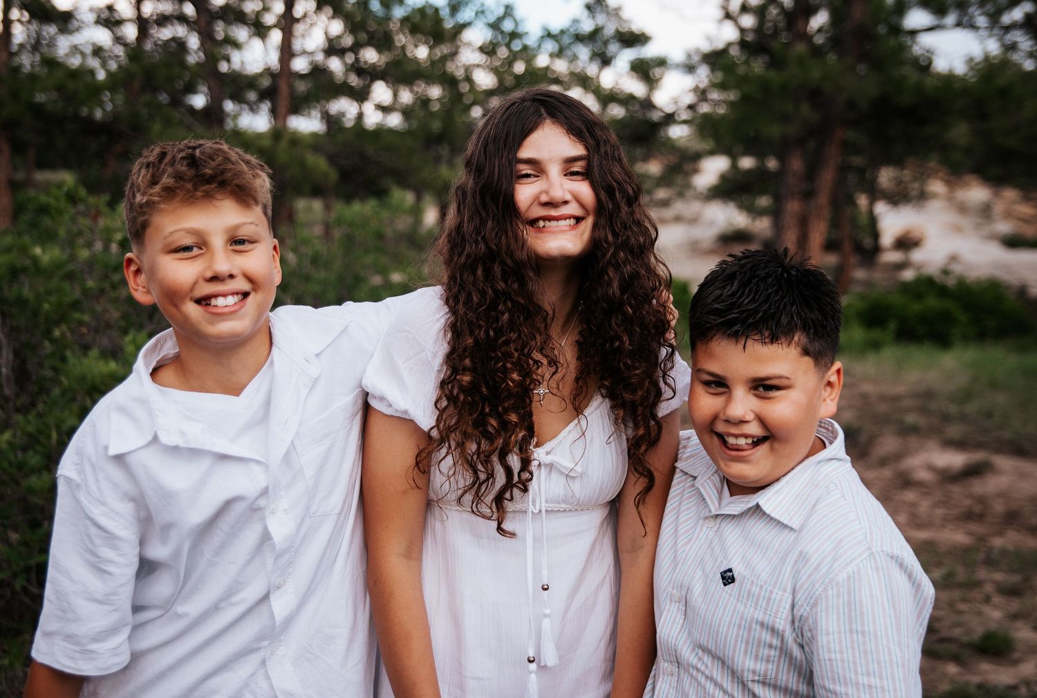 Three siblings in white outfits share genuine laughs during an outdoor photoshoot at Ute Valley Park in Colorado Springs