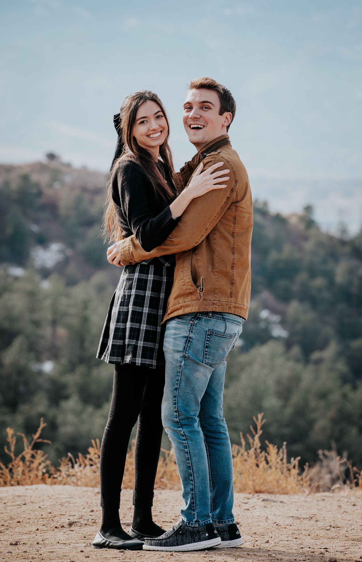 A romantic scene unfolds as a couple embraces on a hilltop with mountains in the background.