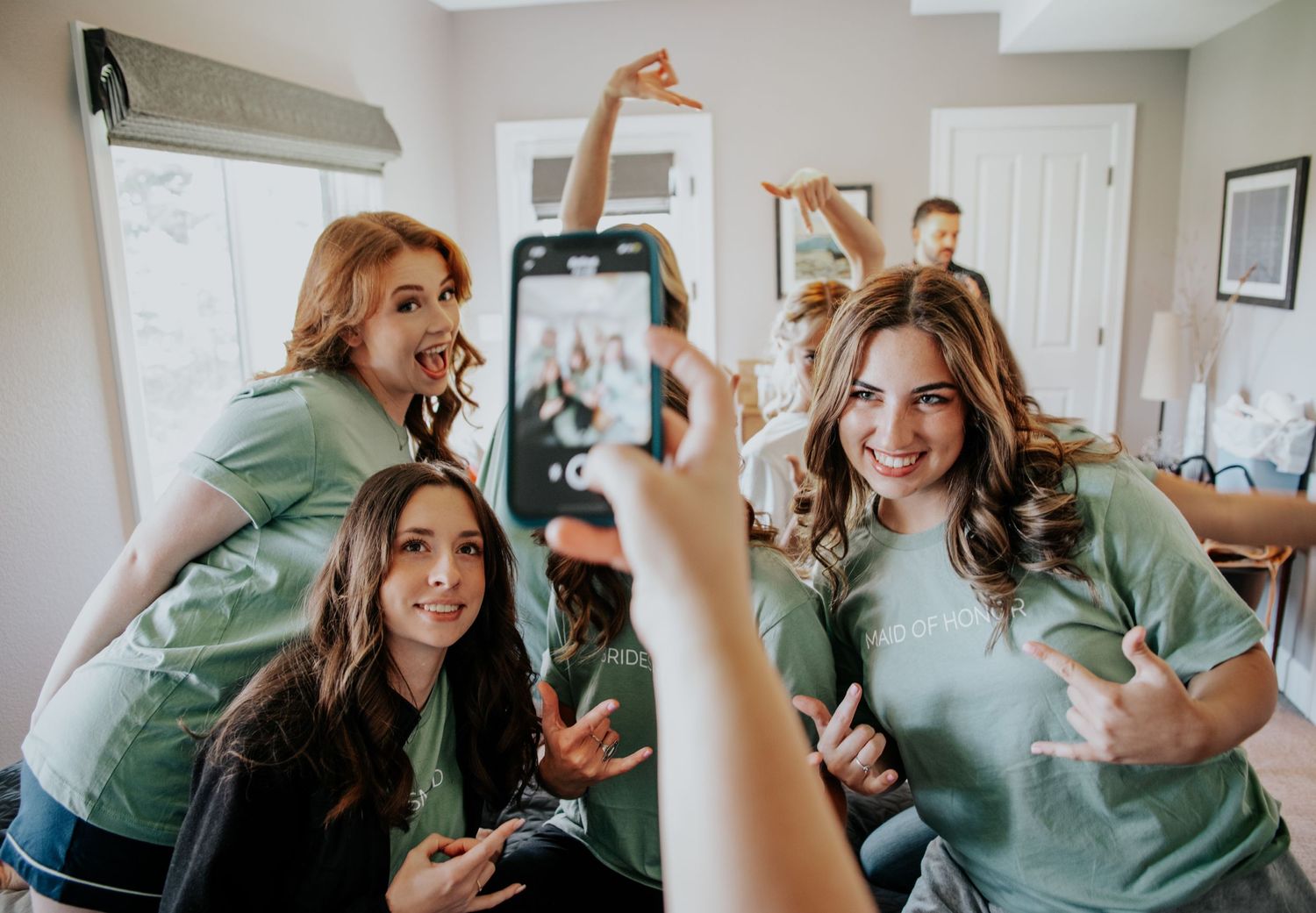Group in matching mint green shirts taking selfies and celebrating together.