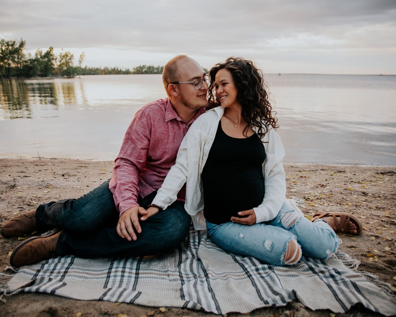 Couple relaxing together on a plaid blanket at the beach during sunset.