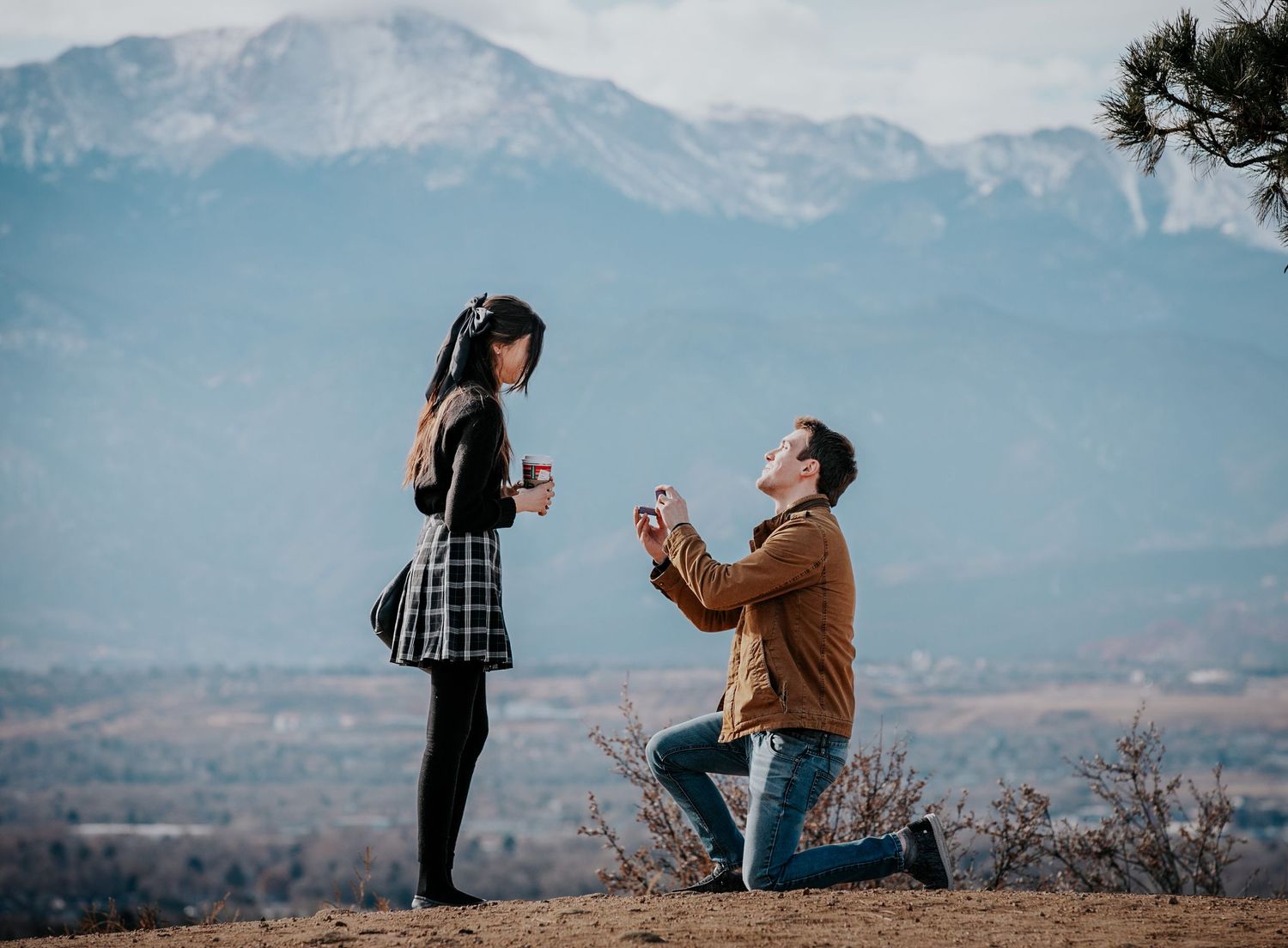 Marriage proposal taking place on scenic overlook with mountains and valley below.