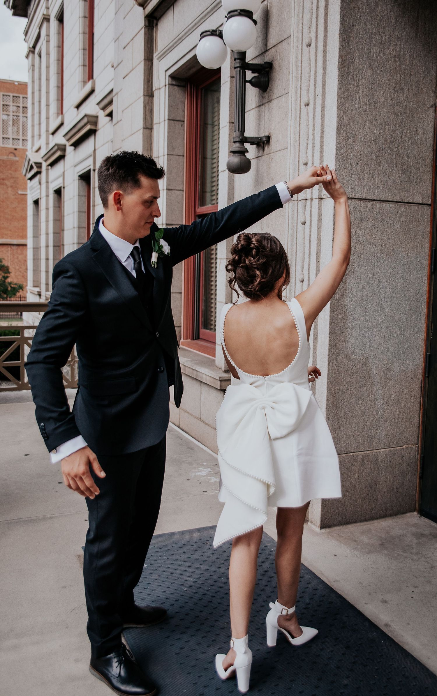 A couple dancing playfully in a city street, with the bride in a short white dress and groom in a black suit.