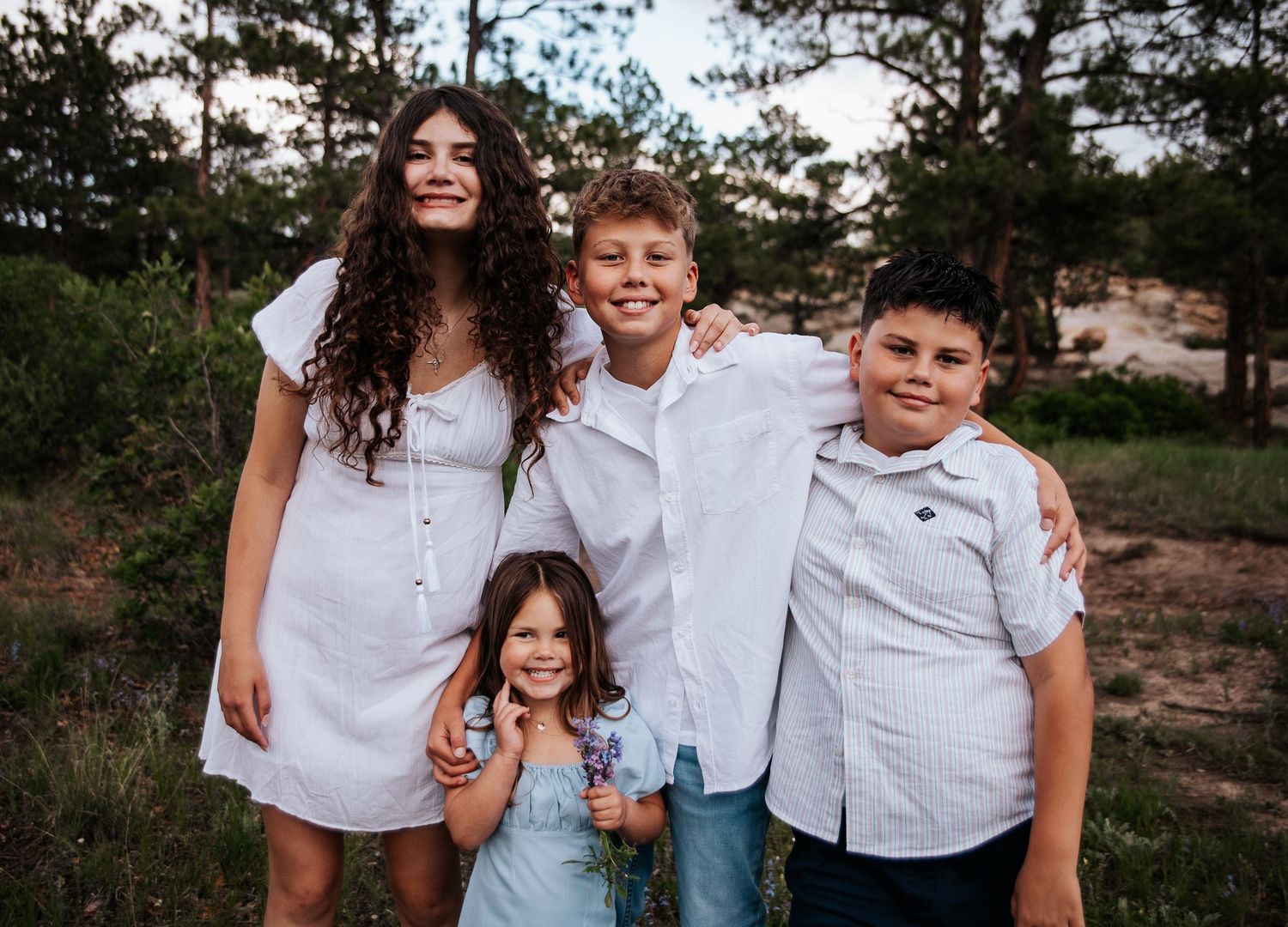 Four siblings wearing coordinated white outfits pose together outdoors at sunset at Ute Valley Park in Colorado Springs