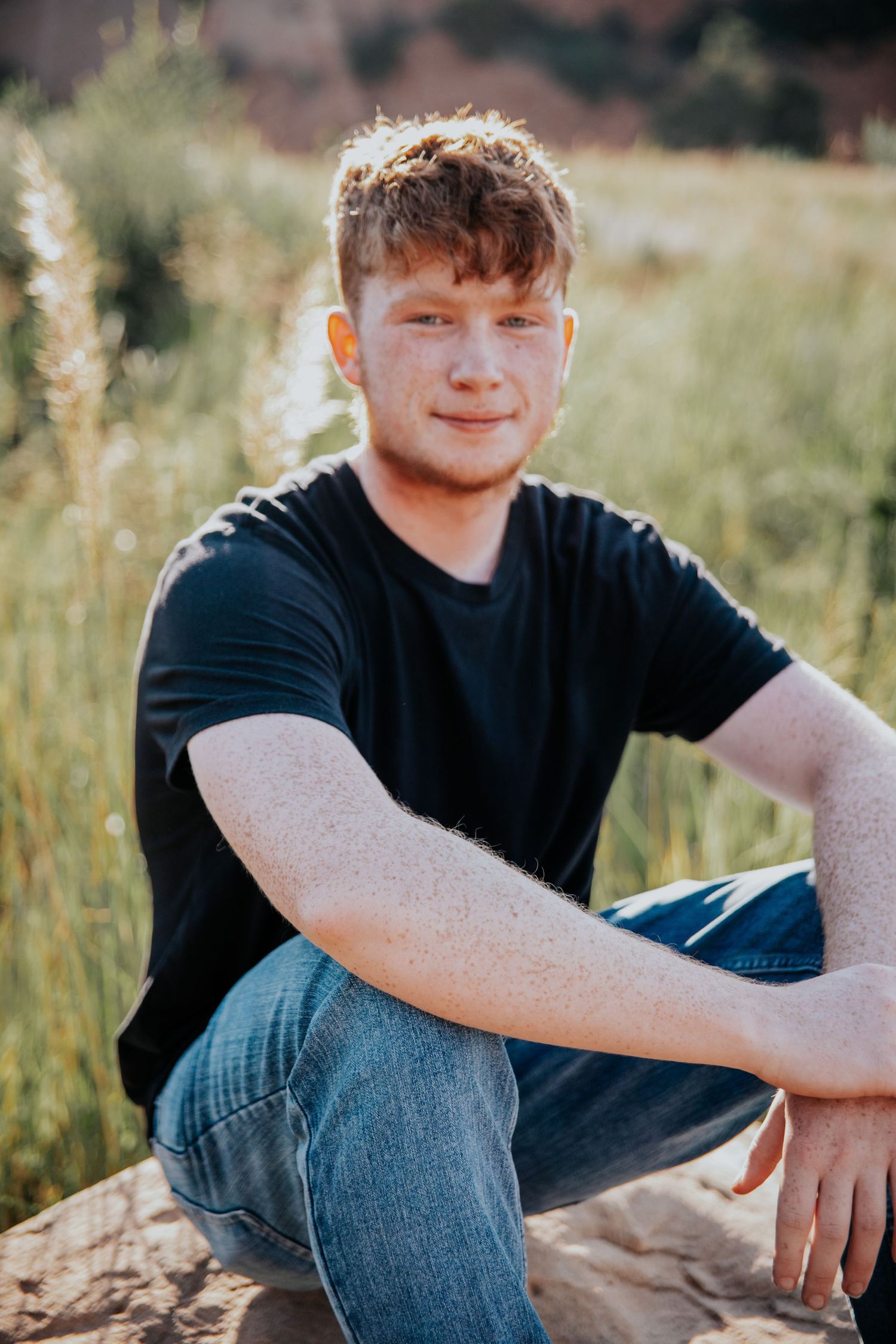 Portrait session in a grassy field during golden hour light wearing a black t-shirt and jeans.
