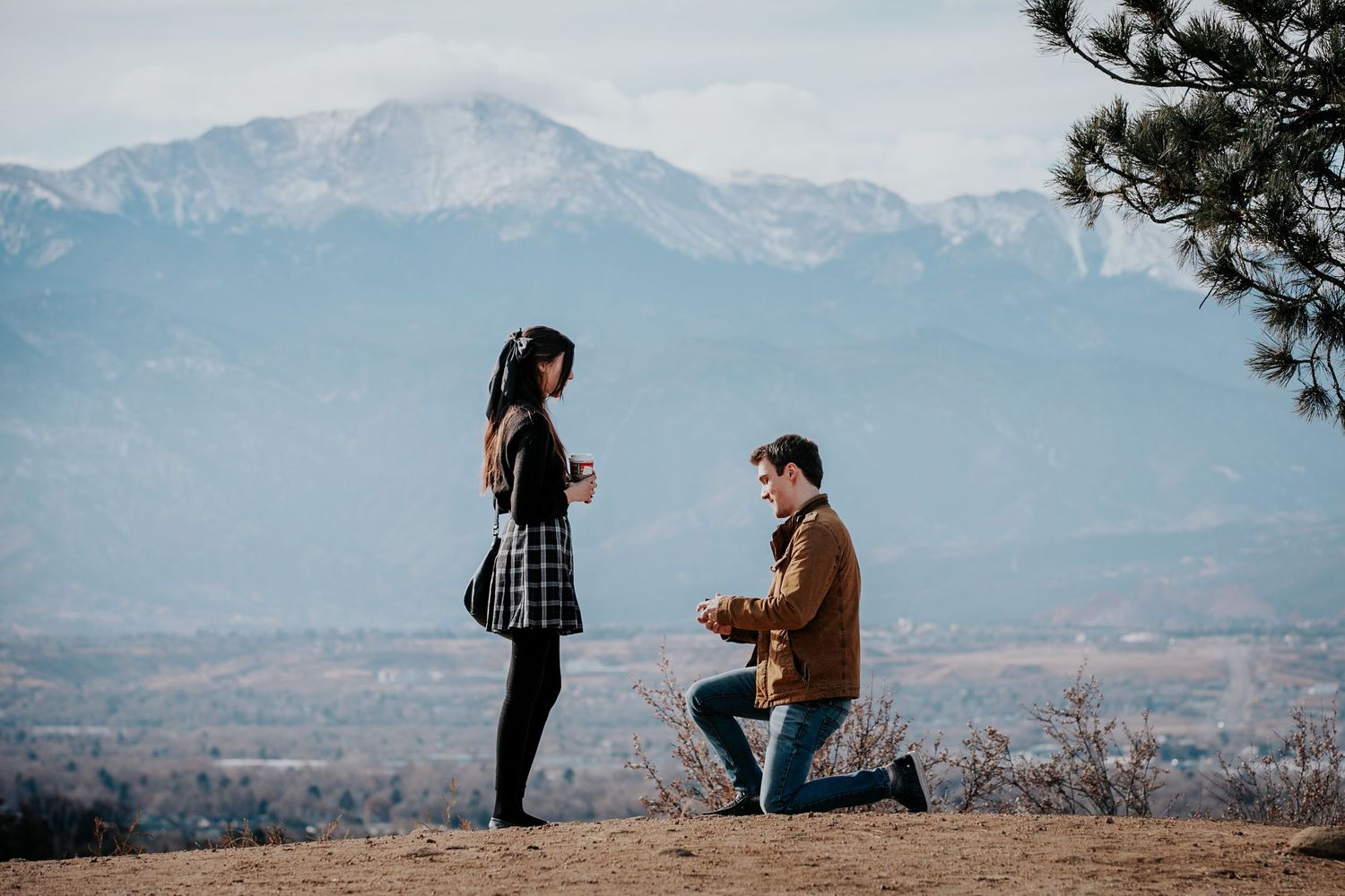 Proposal moment captured on hilltop with stunning mountain range in background.