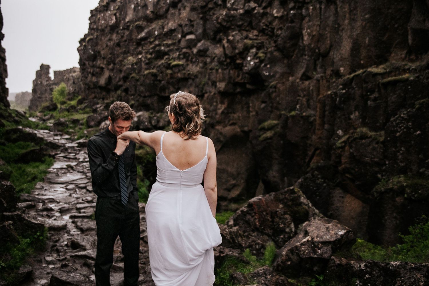A couple explores dramatic rocky cliffs in elegant wedding attire.