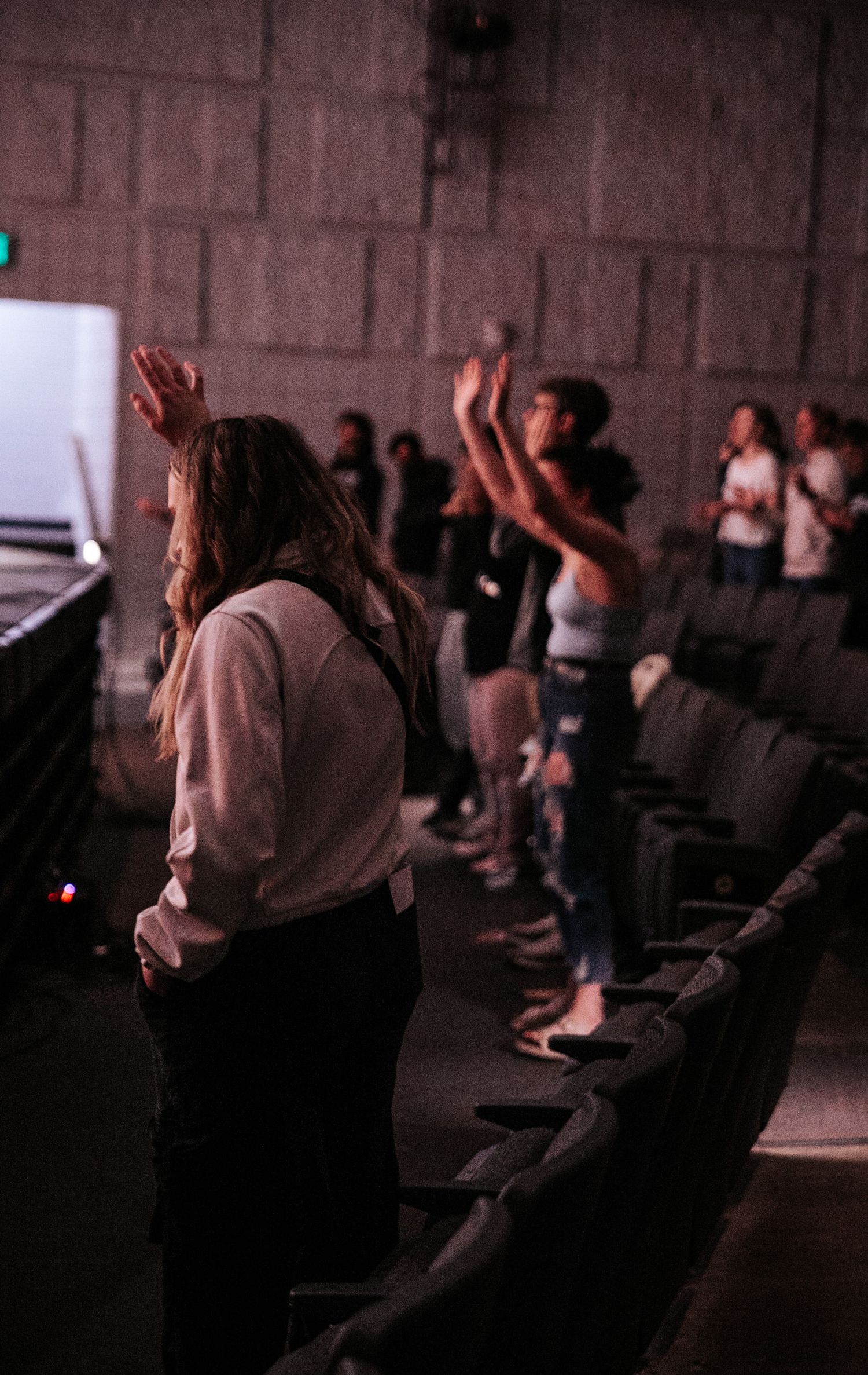 Audience members raise their hands in a darkened theater.