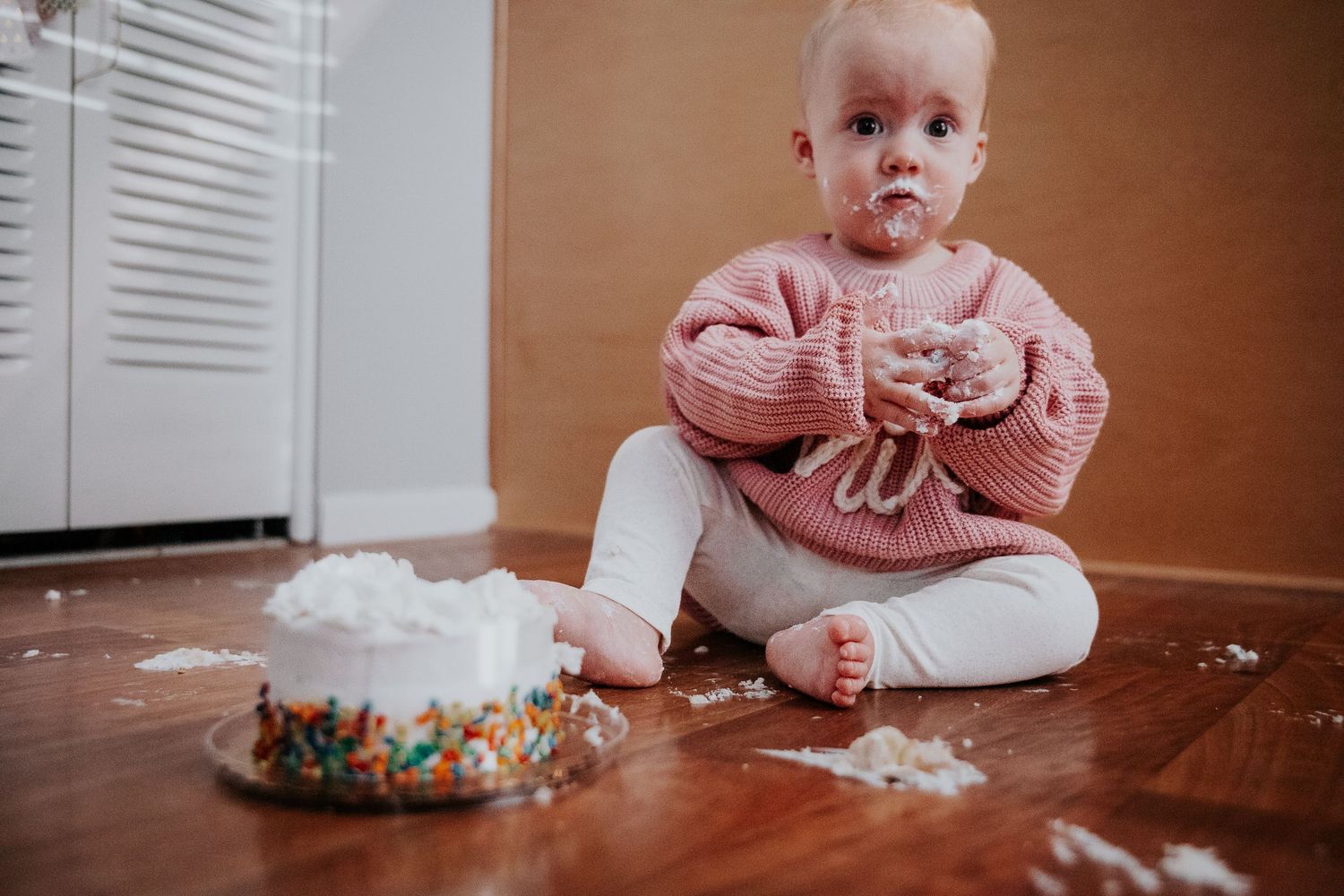 A first birthday cake smash scene with pink decorations and white frosting scattered on floor.