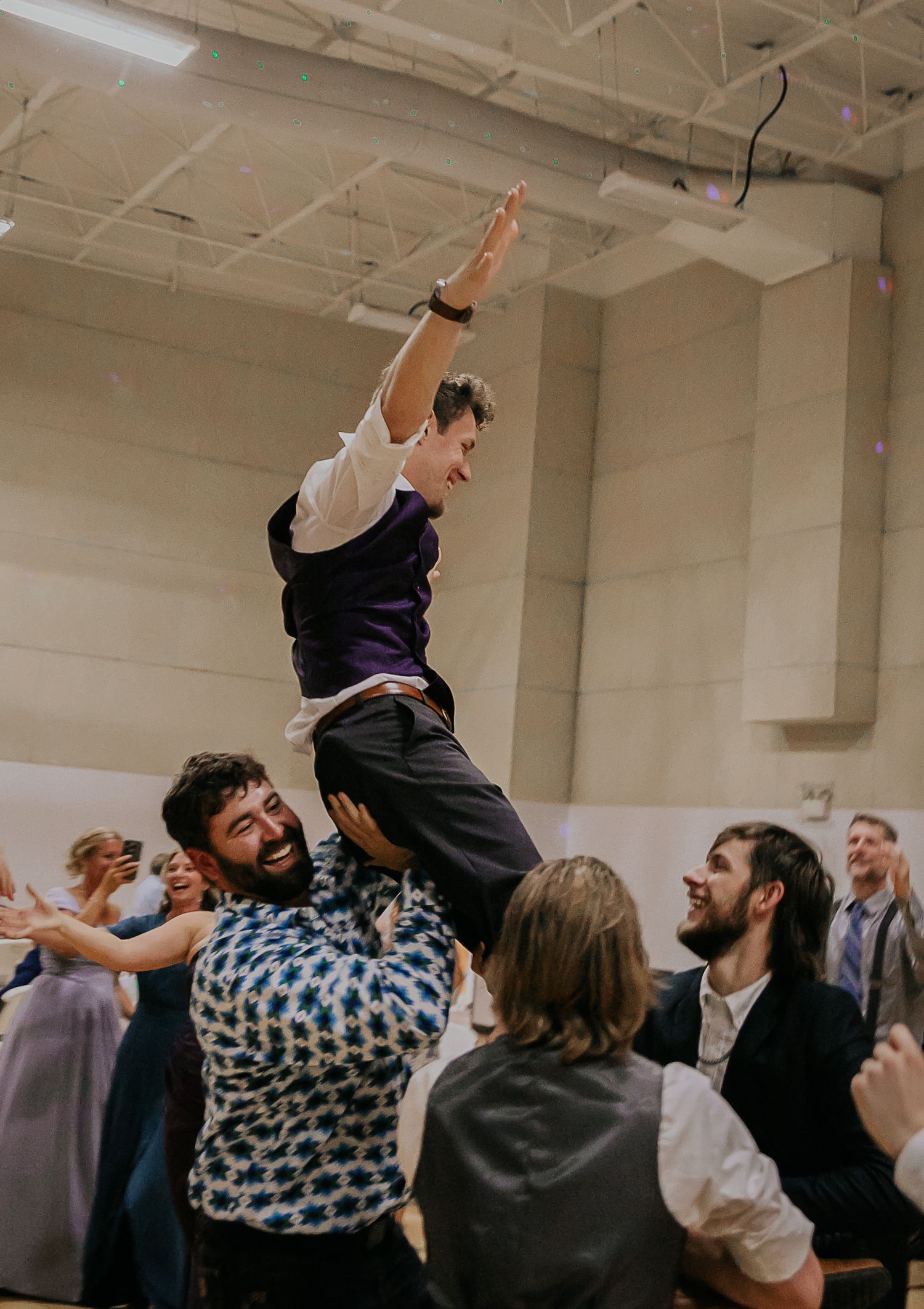 A celebratory moment at a wedding reception with someone being lifted high above the crowd.
