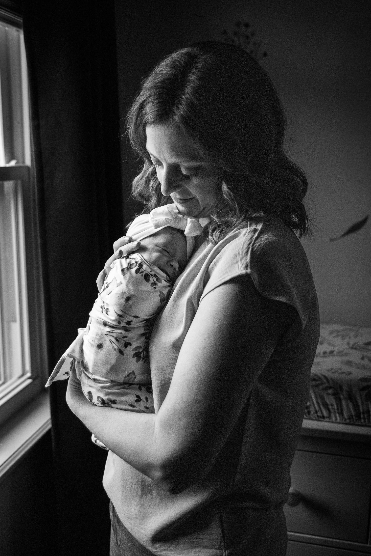 A tender black and white photo series showing a parent embracing a baby near a window.