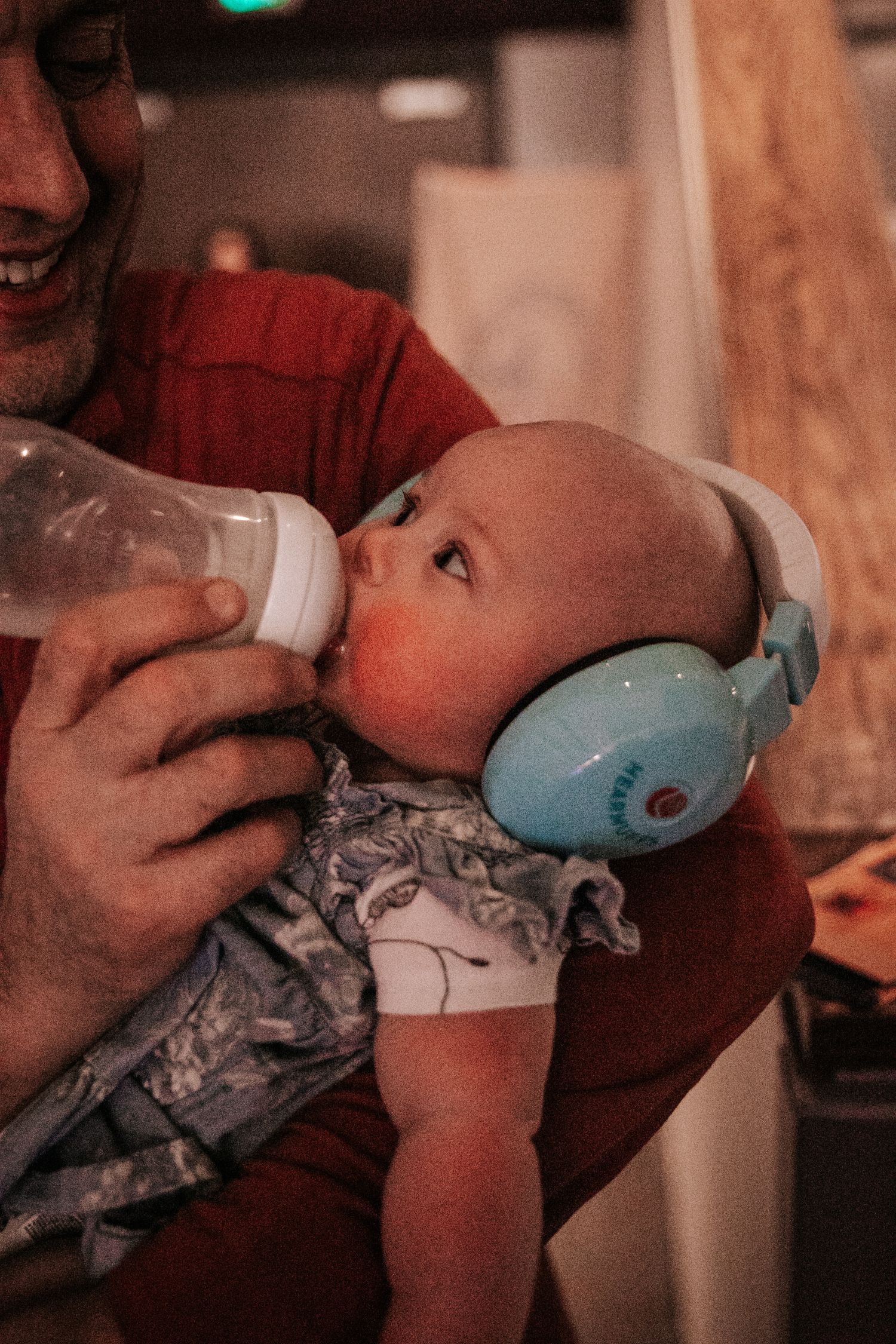Close-up of an infant wearing blue noise-canceling headphones while drinking from a bottle.