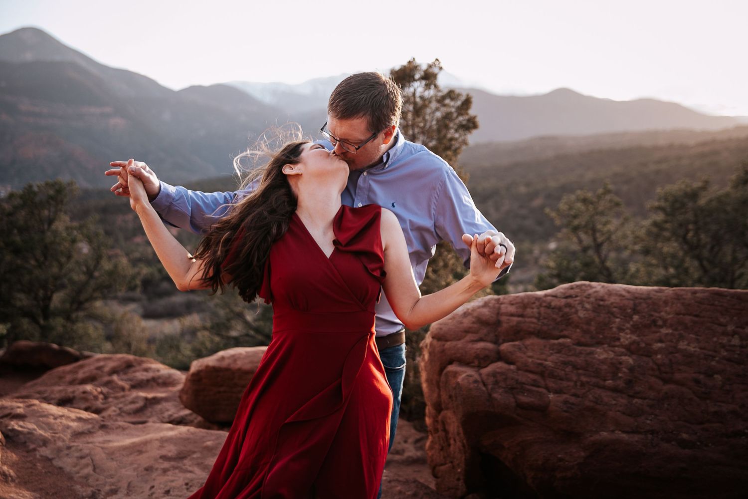 A couple dancing on red rocks with mountains and desert landscape in the background.