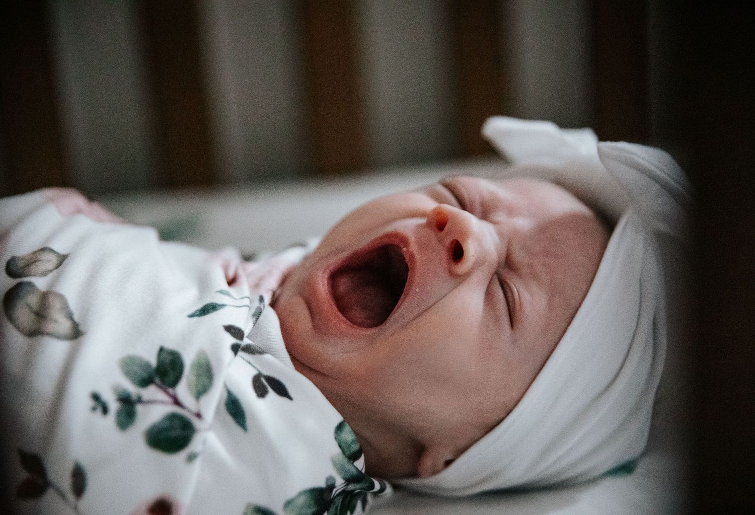 A sleeping baby in white clothing with floral print lies on white bedding.