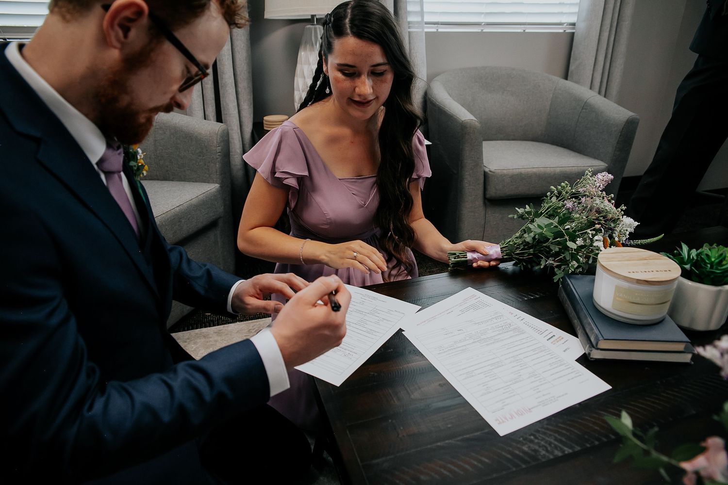 People reviewing and signing wedding documents at a table with flowers and teacups.