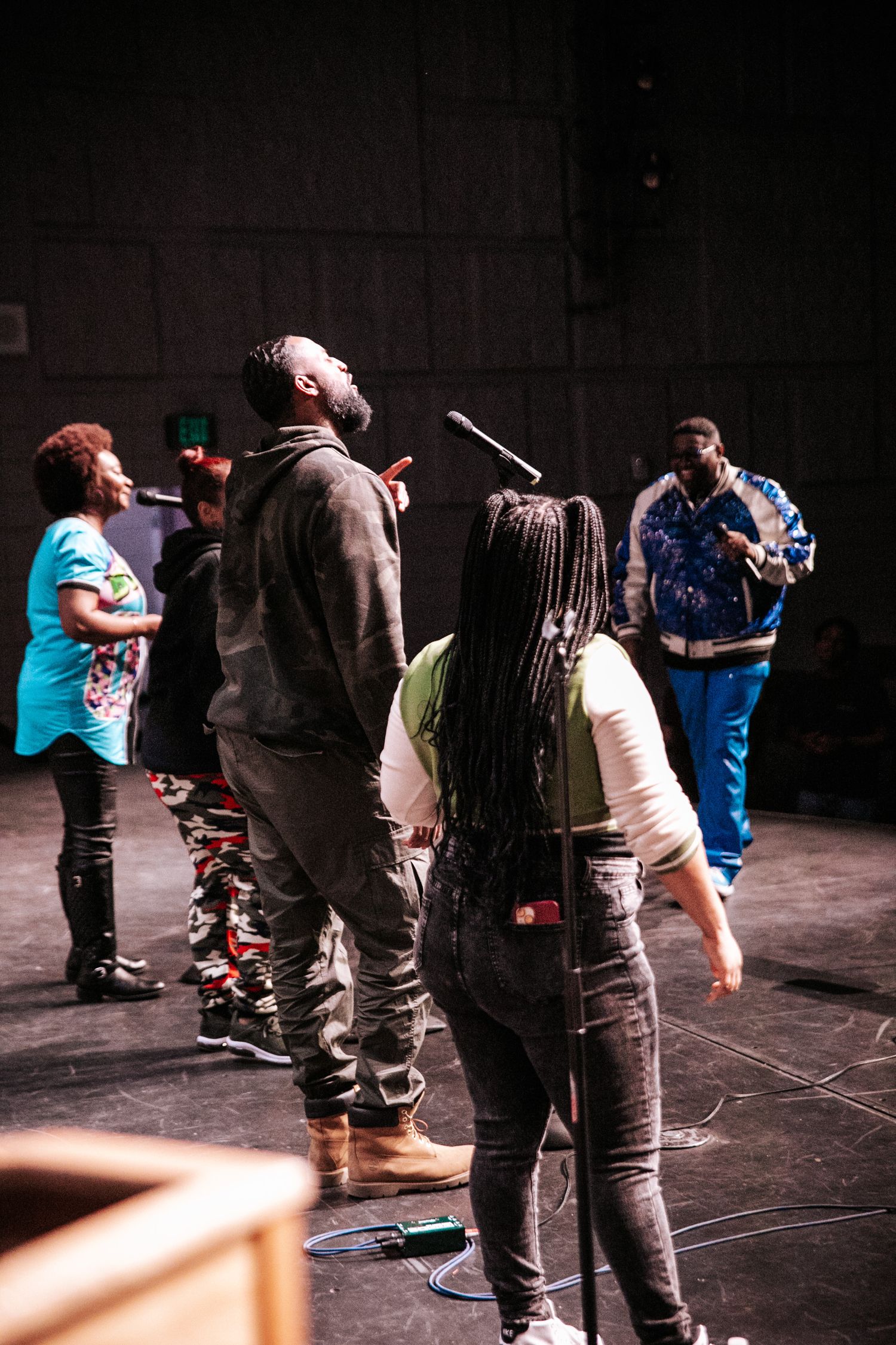 Group of performers in casual attire standing on a dimly lit stage.