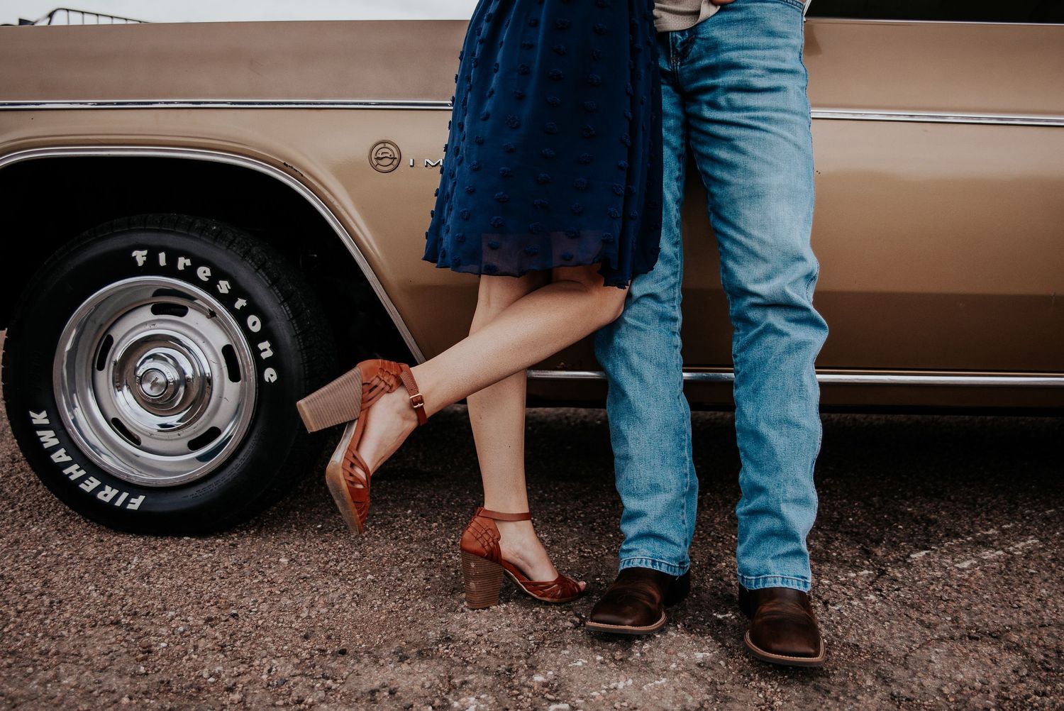 Couple's legs visible next to vintage car wheel showing contrasting formal and casual footwear.