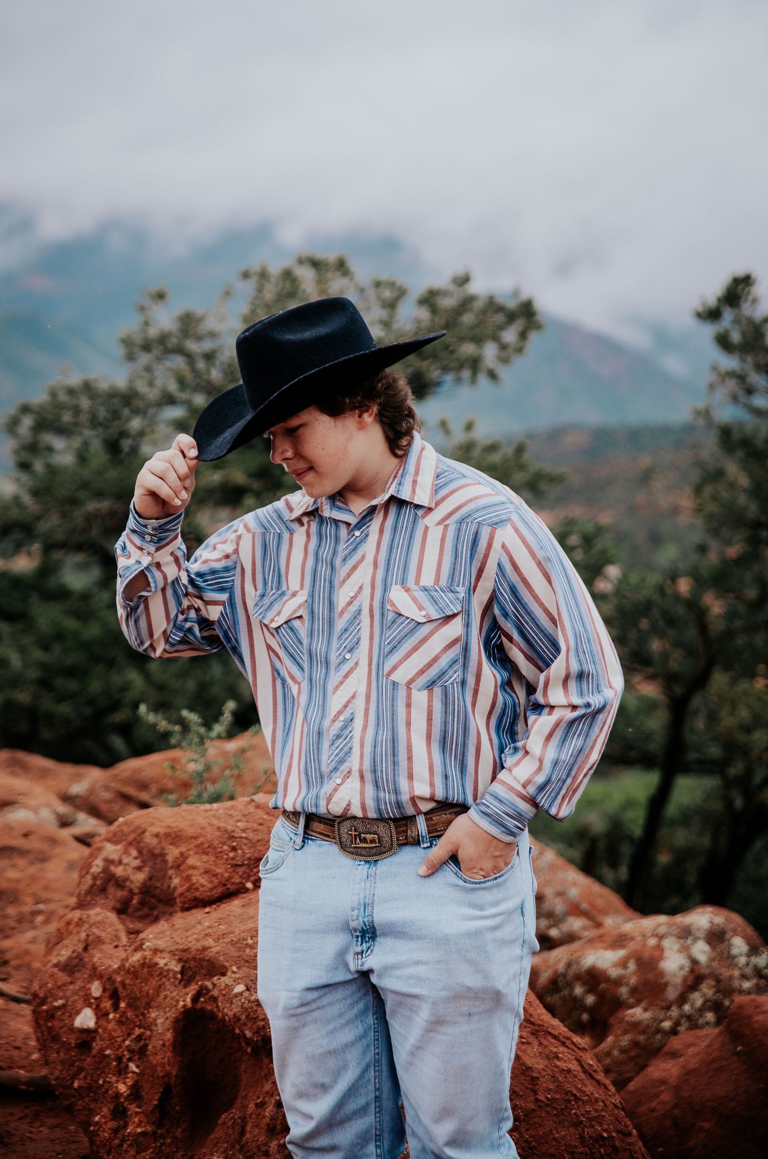 A high school senior in western wear sits casually on red rock formations at Garden of the Gods in Colorado Springs