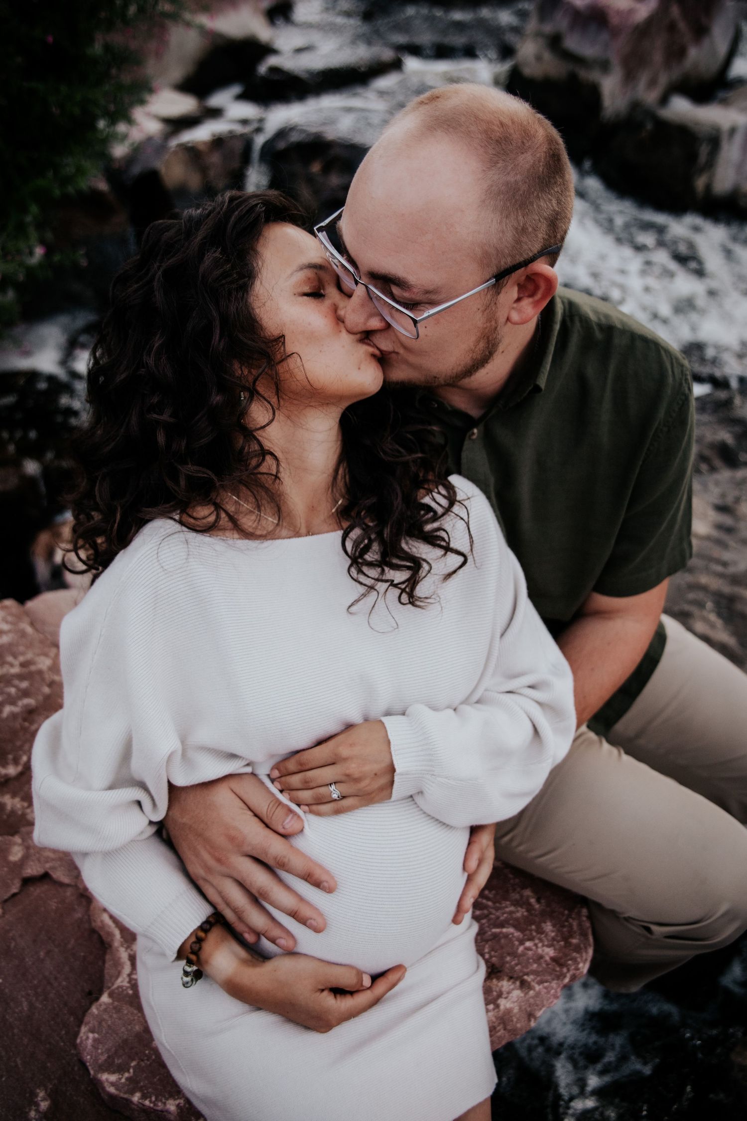 Romantic maternity photos on rocky terrain with couple embracing.