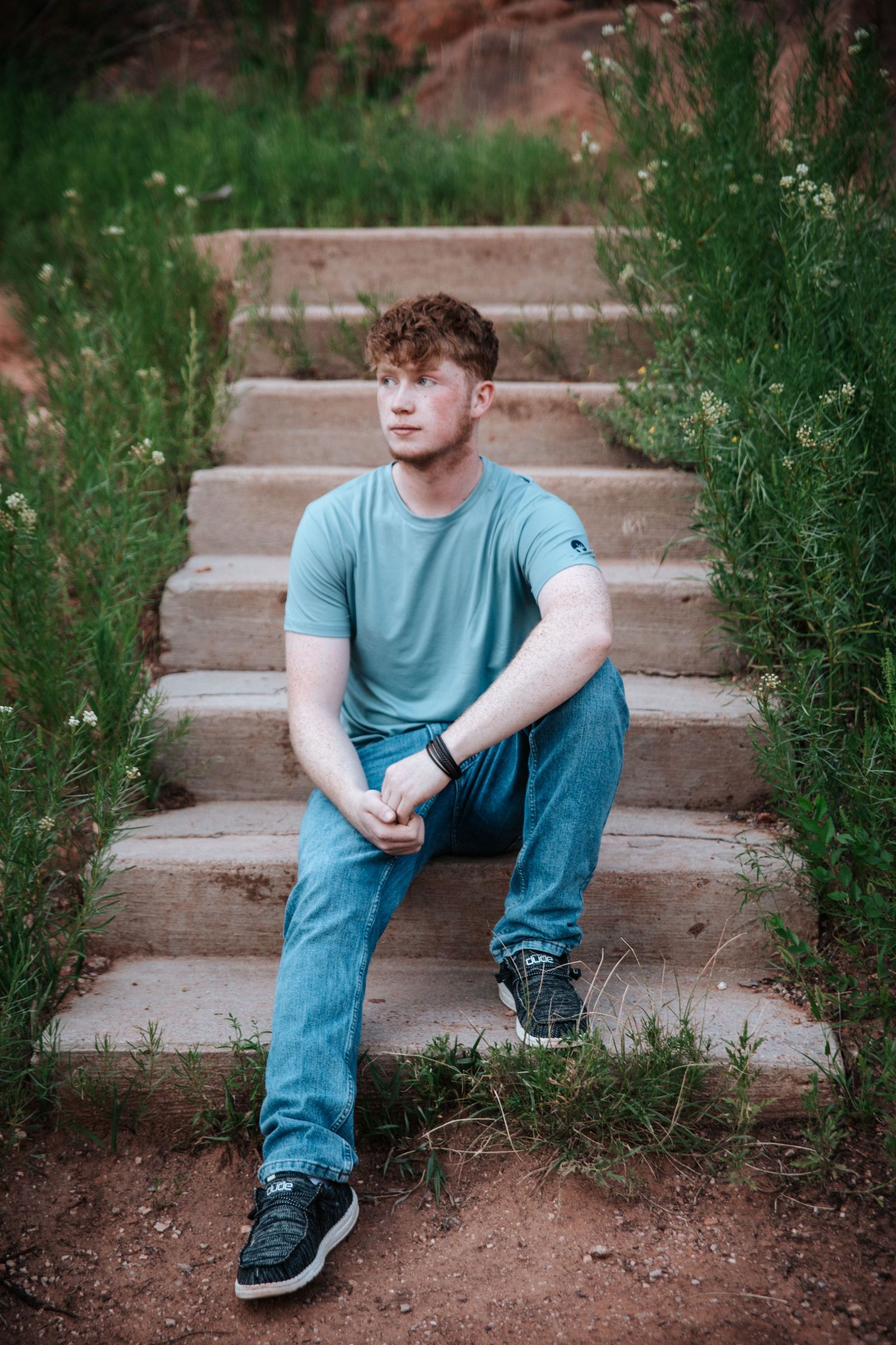 Person sits on stone steps surrounded by greenery and red rock formations.