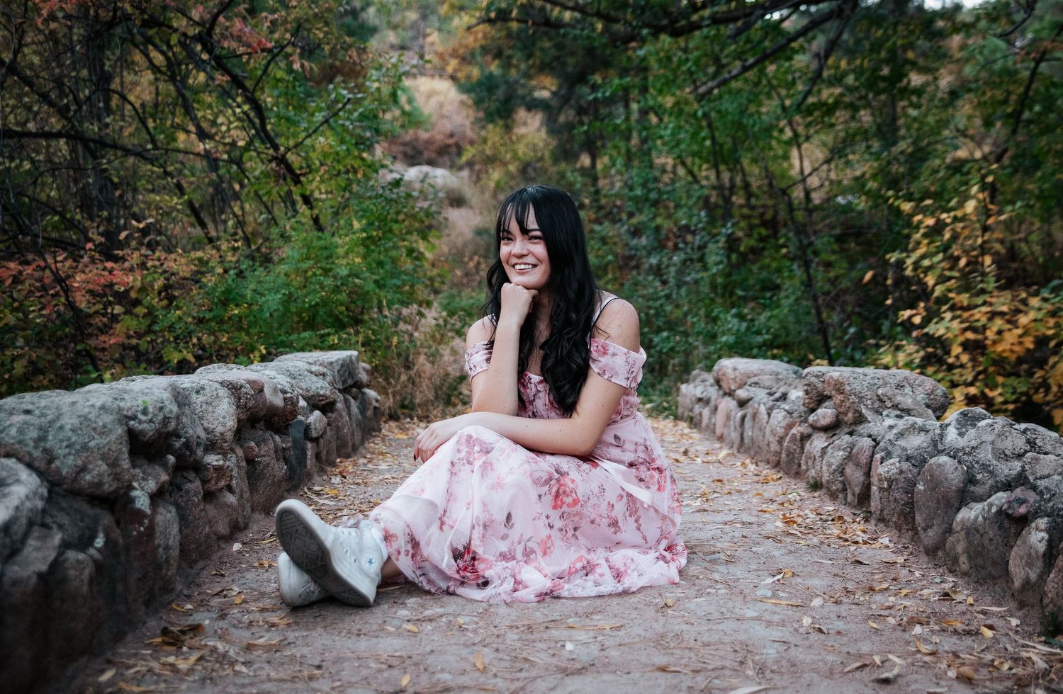 A stone-lined path creates a romantic backdrop for a flowing pink dress photoshoot.