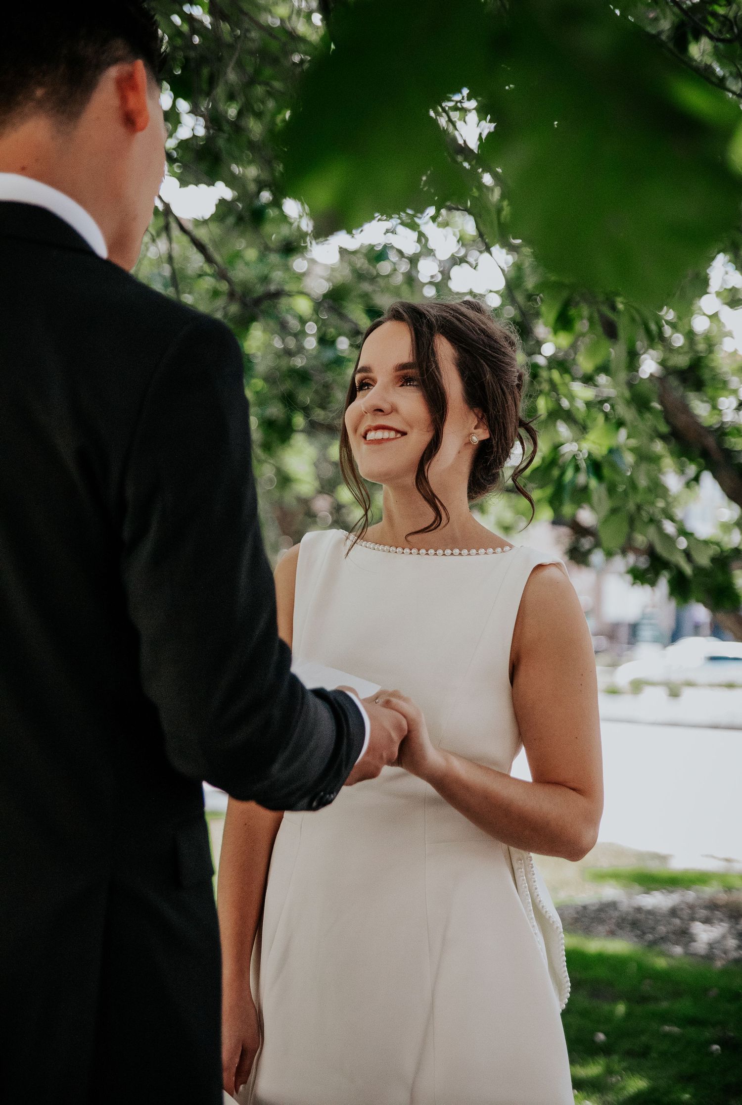 A couple in formal wedding attire shares joyful laughter under green tree branches at Colorado Springs courthouse wedding.
