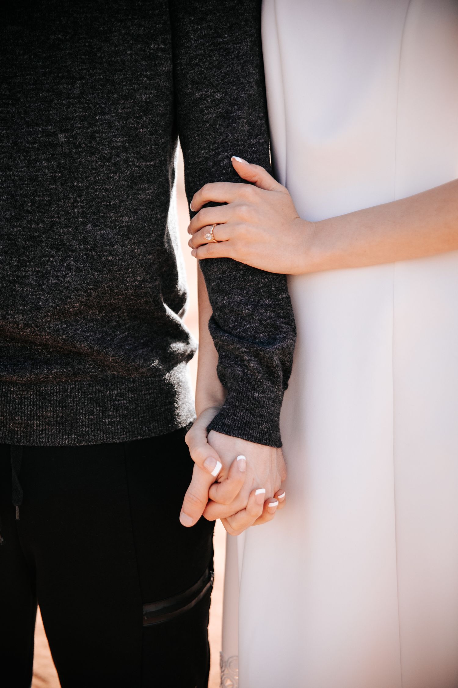 Close-up detail of hands touching and holding between two people in contrasting outfits.