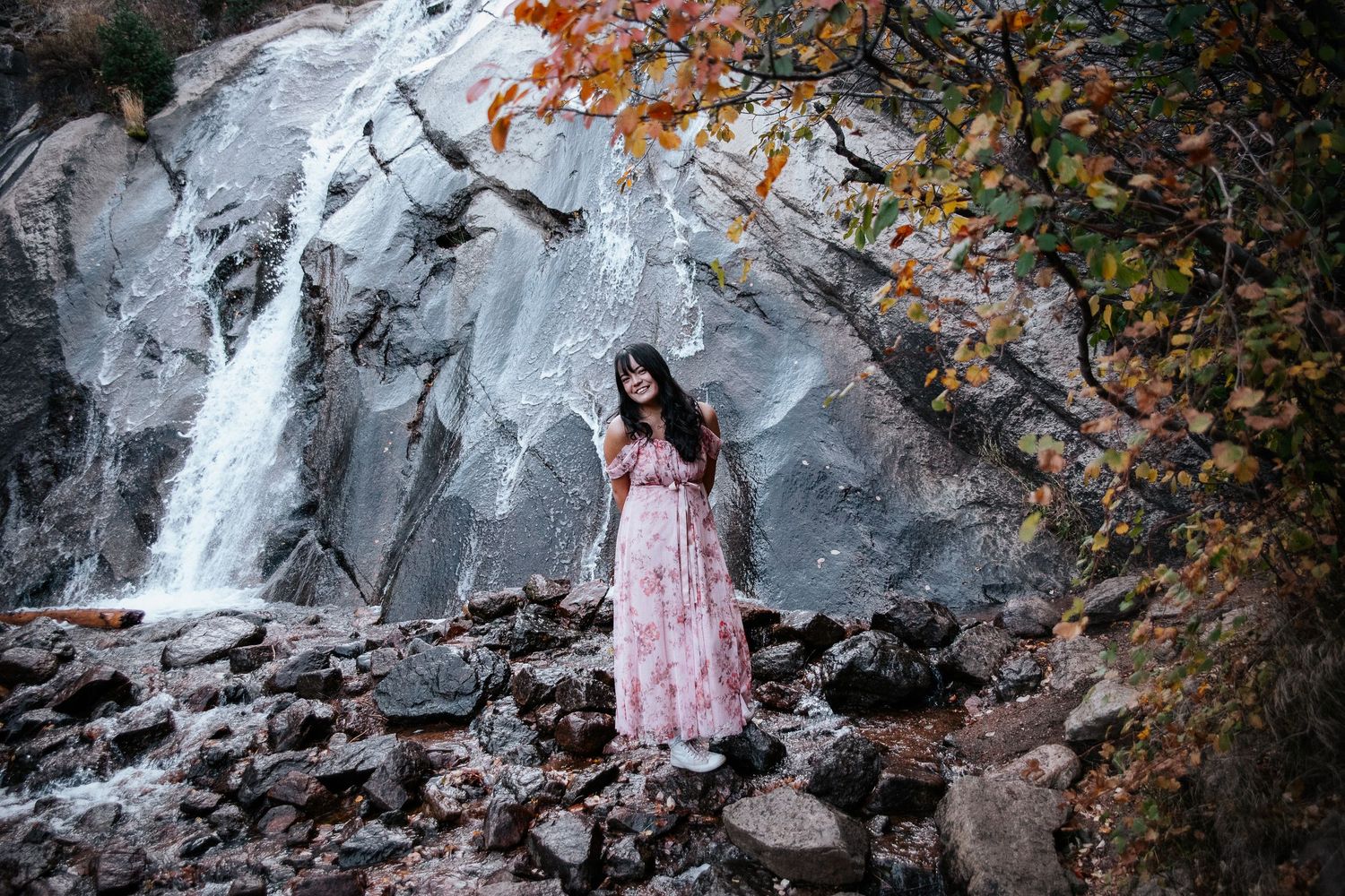 A pink floral dress contrasts against a dramatic rocky waterfall backdrop.