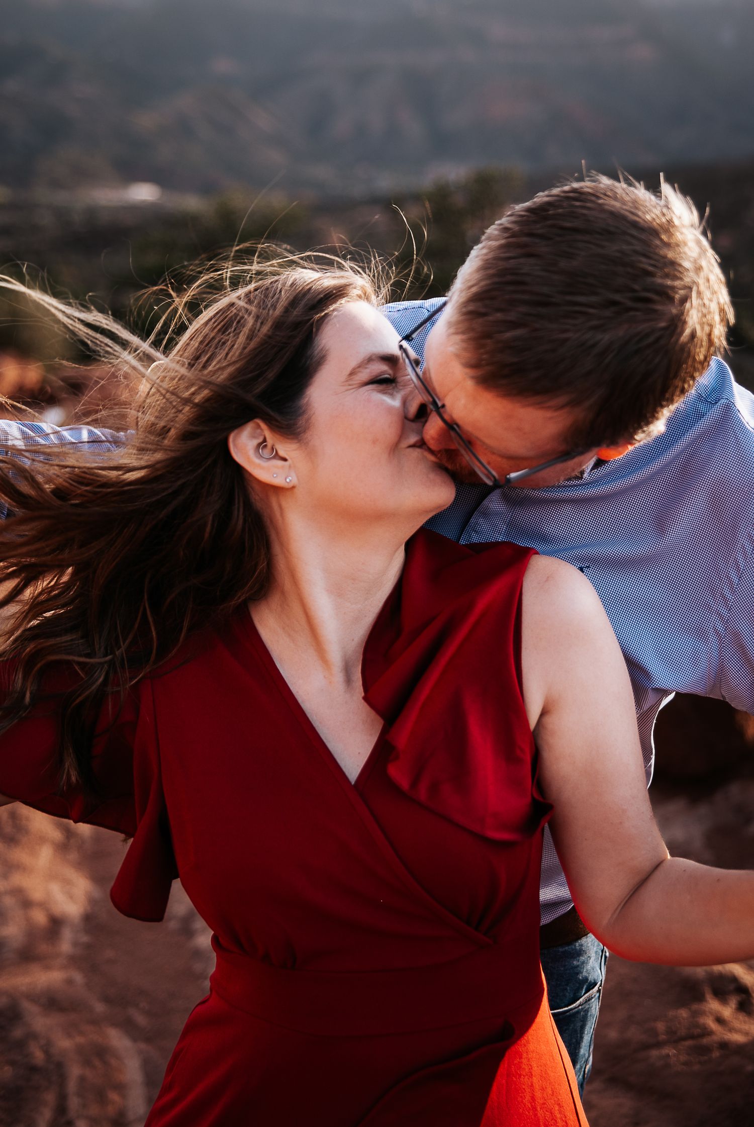 A romantic couple shares a tender kiss against a mountainous backdrop at sunset.