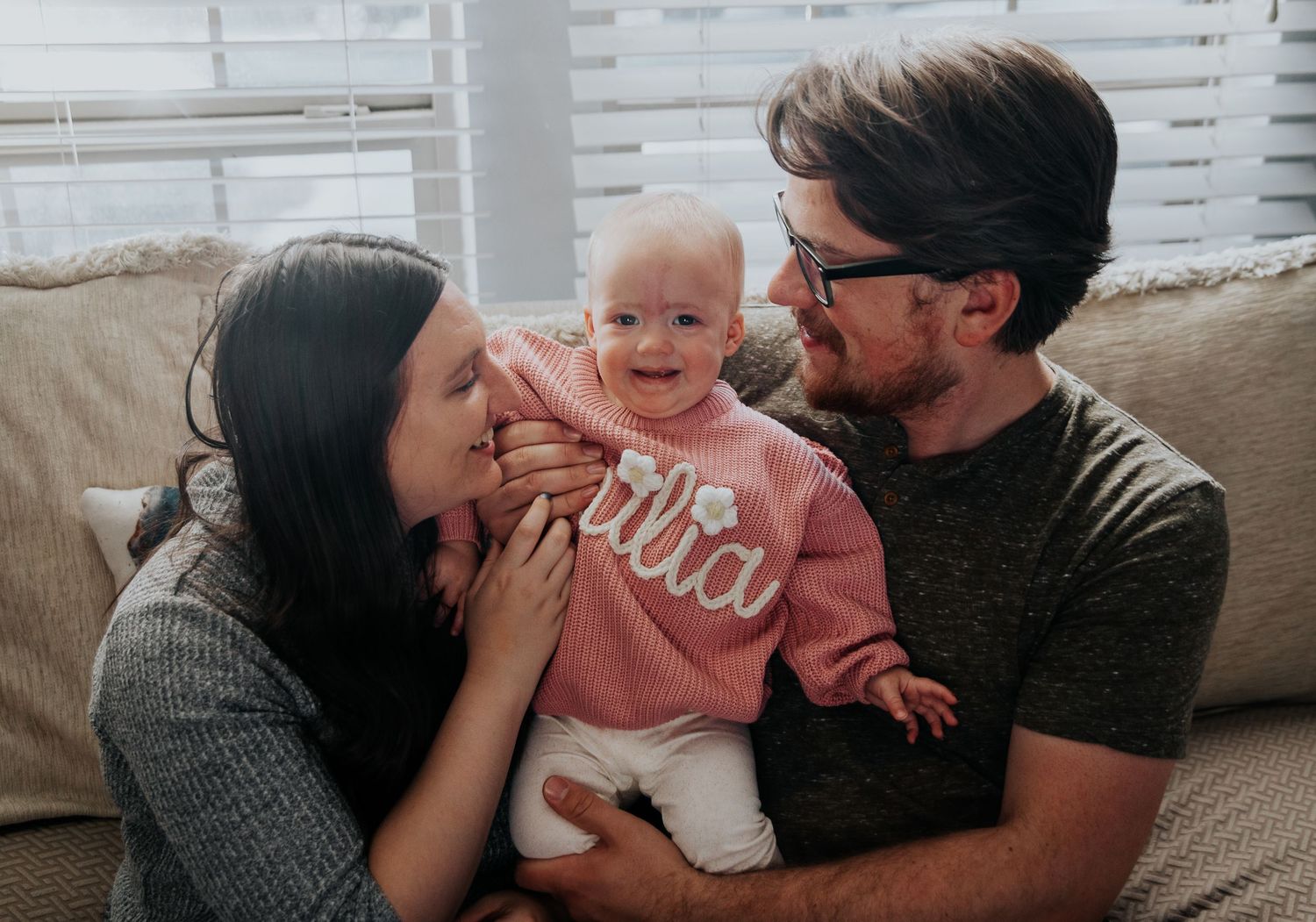 Family cuddles and plays together on grey couch.