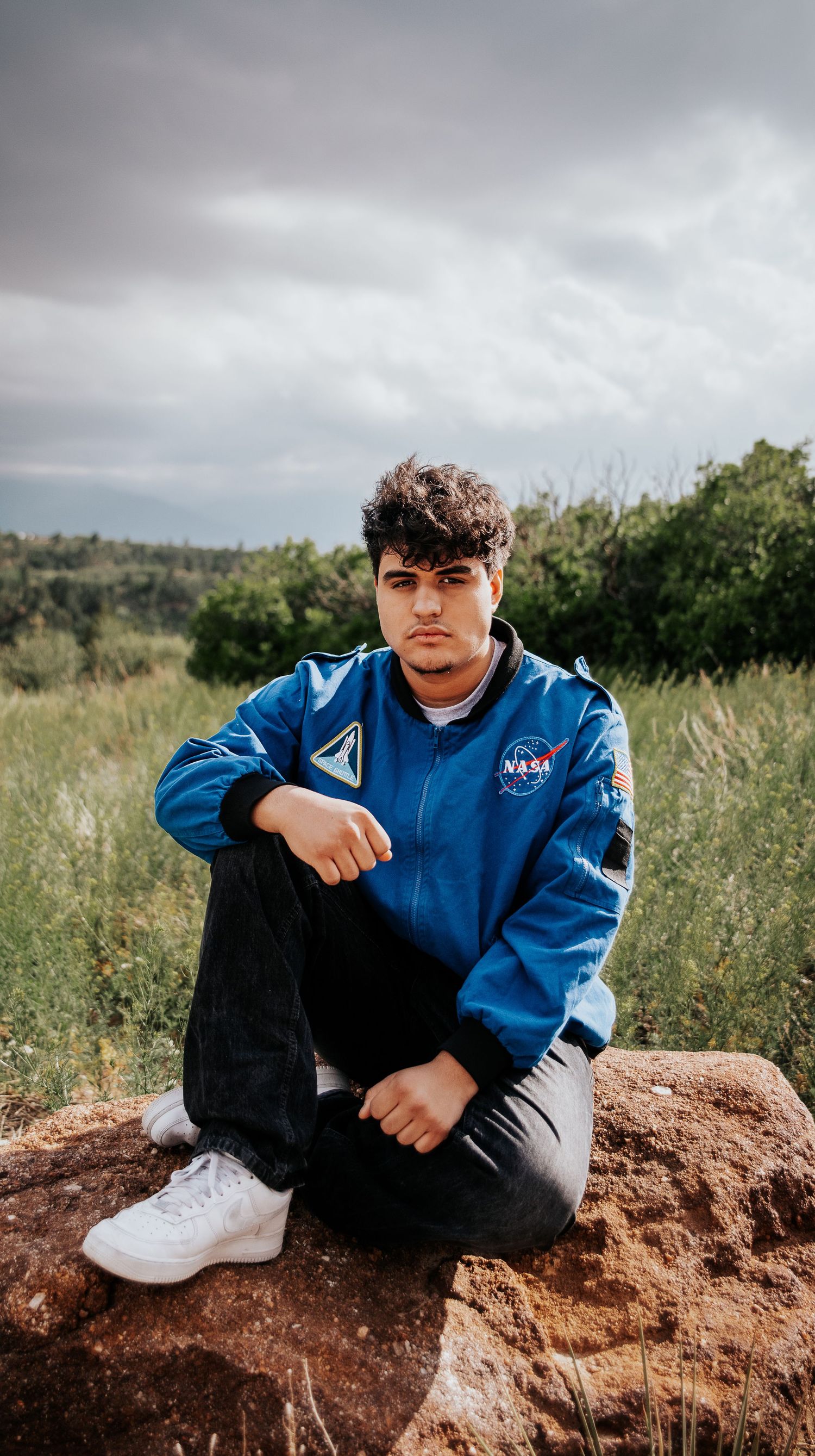 High school senior wearing NASA flight suit sitting on red rock formation surrounded by grass at Palmer Park in Colorado Springs