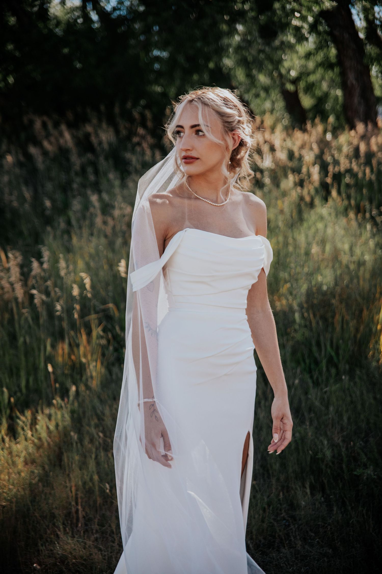 A flowing white wedding dress photographed in golden field at sunset with tall grass and flowers.