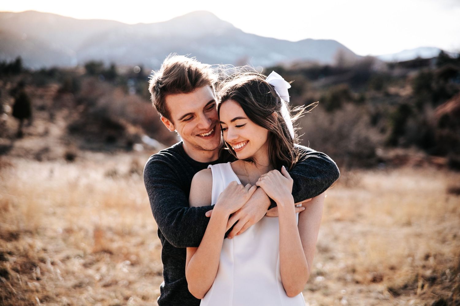 A romantic moment captured between a couple embracing in golden sunlight with mountains in the background.