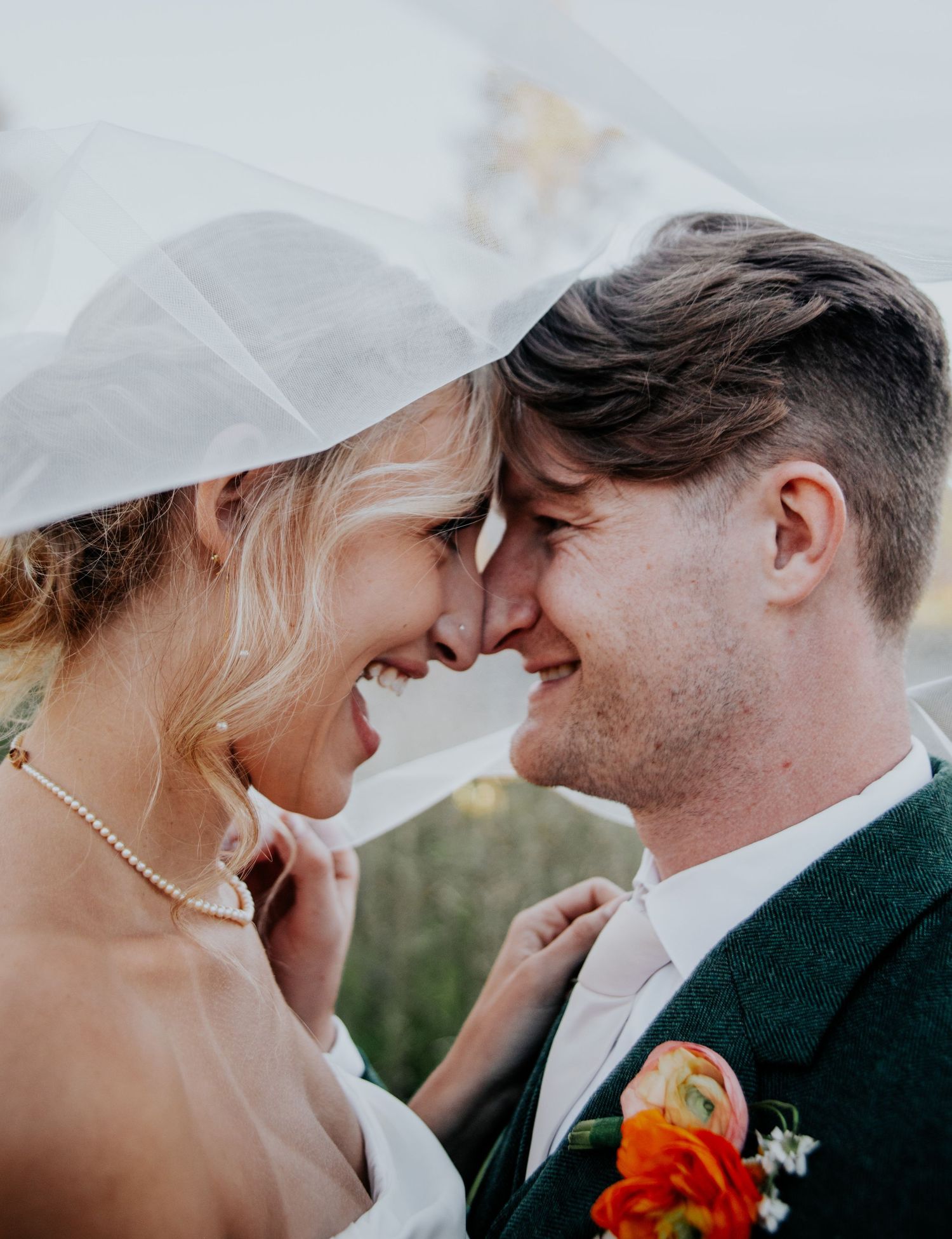 Close-up wedding portrait under white veil with orange floral accents.