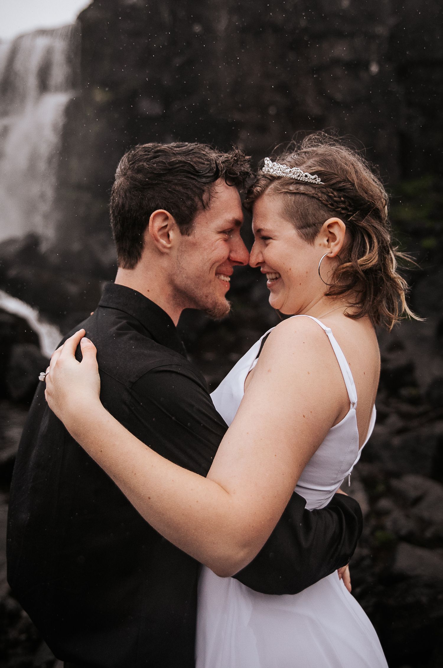 A tender moment captured between a couple as they share laughter in front of a misty waterfall.