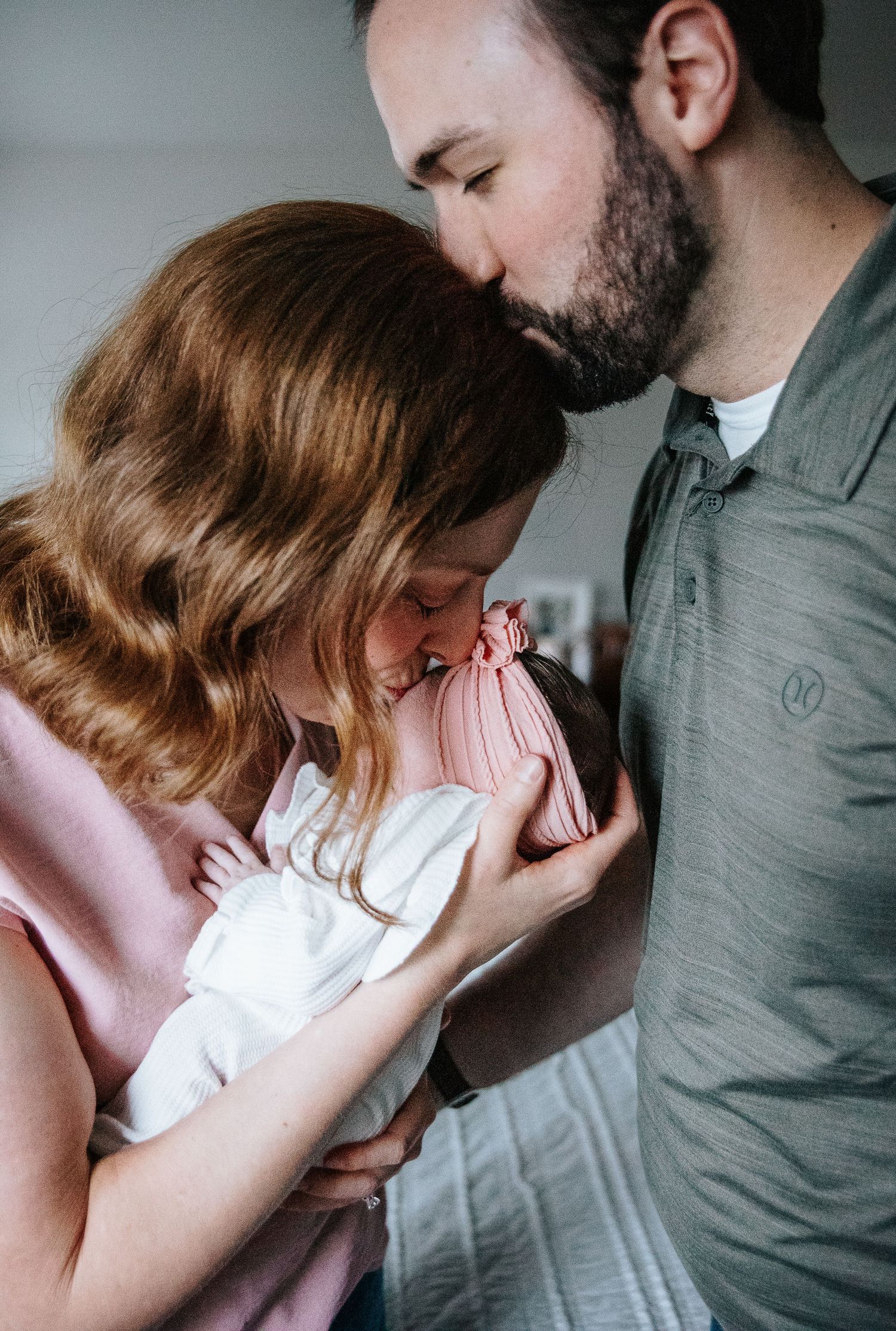 A tender family moment as parents share a quiet embrace with their newborn baby wrapped in white.