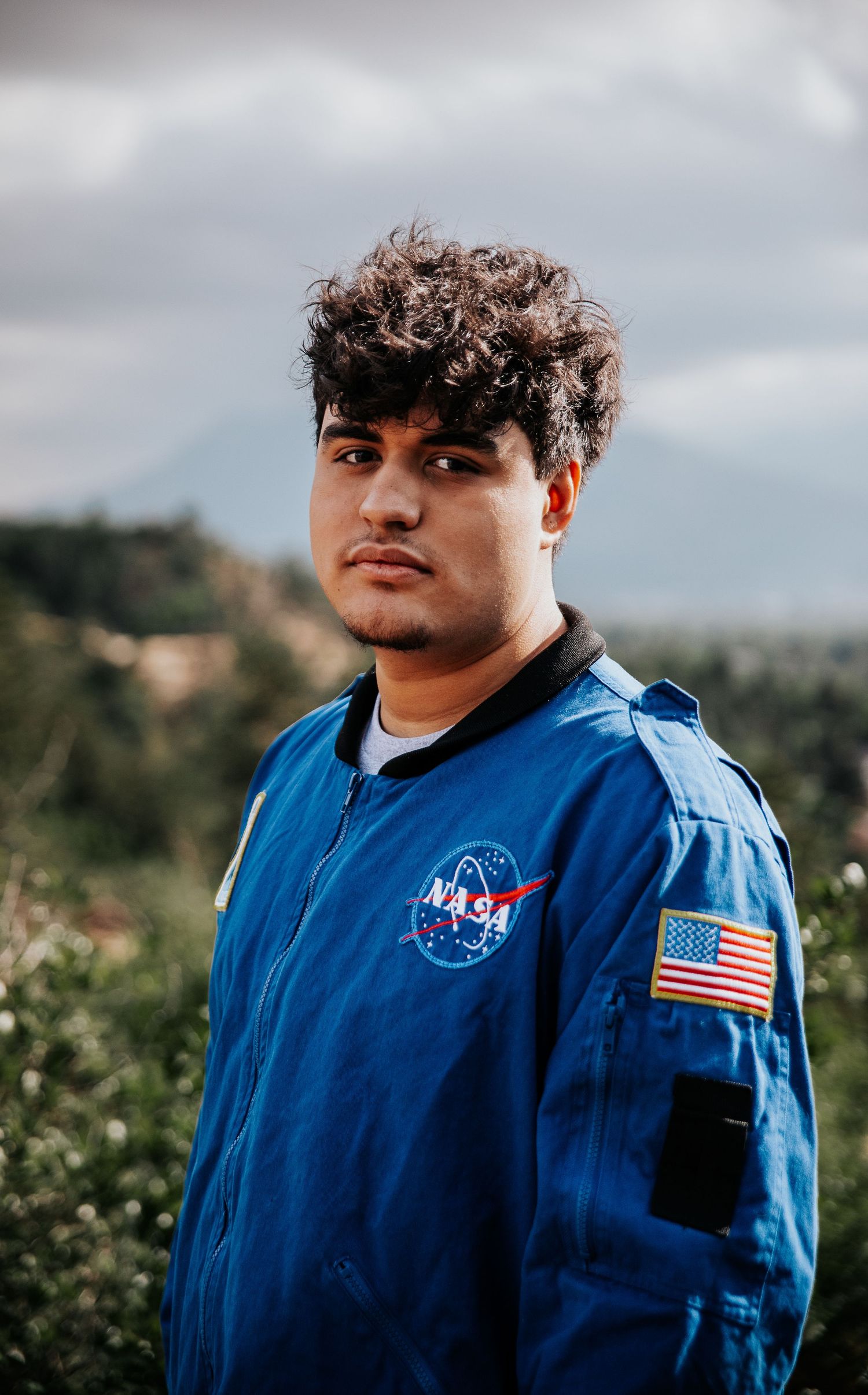 High school senior in official NASA flight jacket with American flag patch poses against natural backdrop at Palmer Park in Colorado Spring