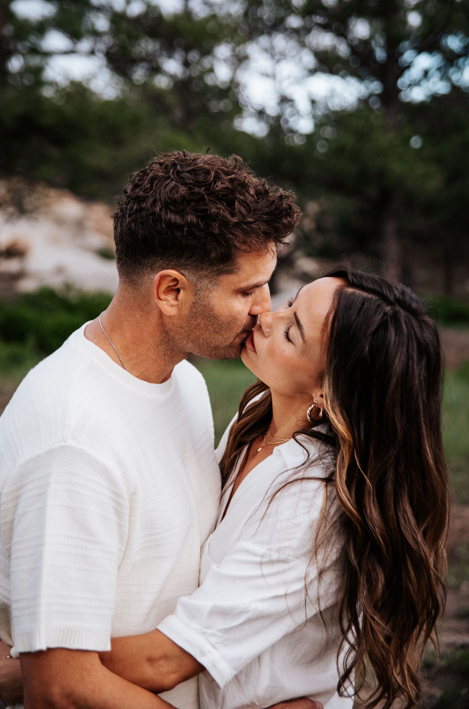 Romantic couple in white shirts share an intimate kiss outdoors at sunset at Ute Valley Park in Colorado Springs