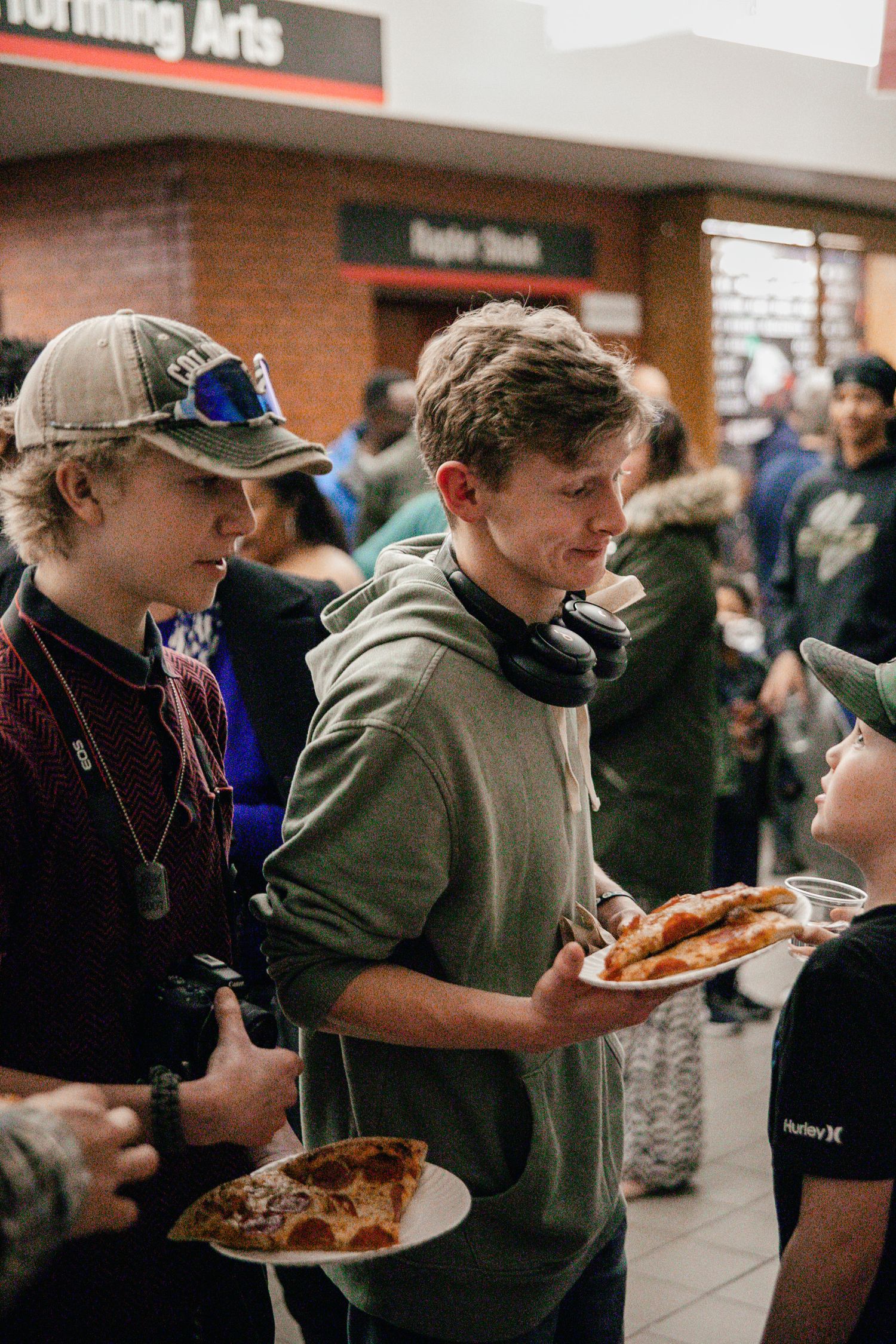 People holding plates of food while standing in line at an indoor event.