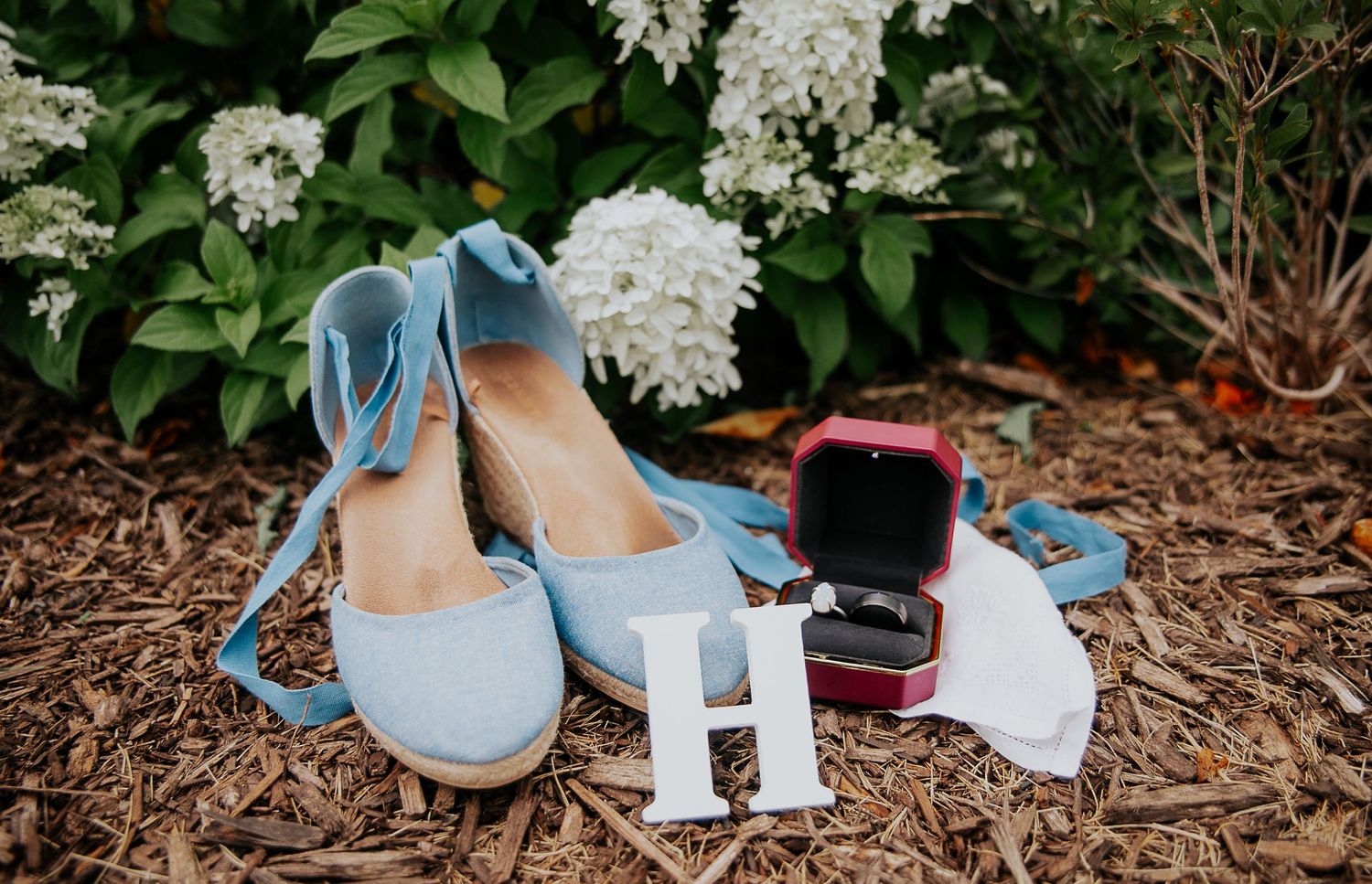 Light blue wedding shoes arranged on brown mulch with delicate white floral details.