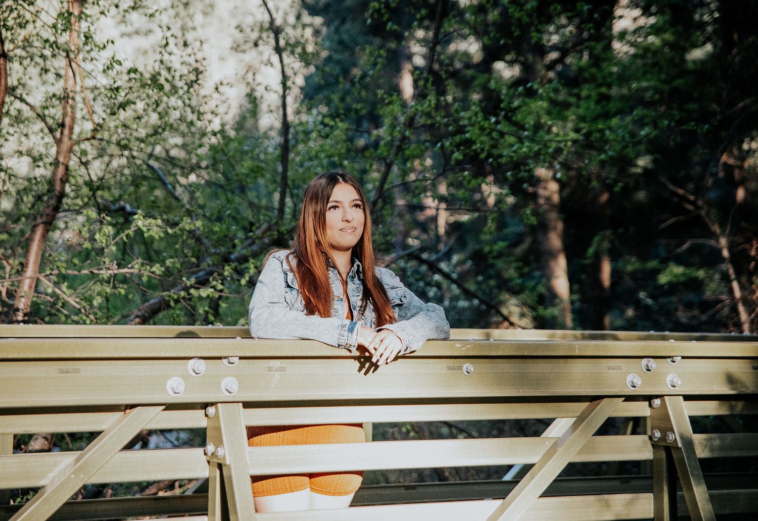 High school senior leaning on wooden bridge railing in forest setting at North Cheyenne Canon in Colorado Springs