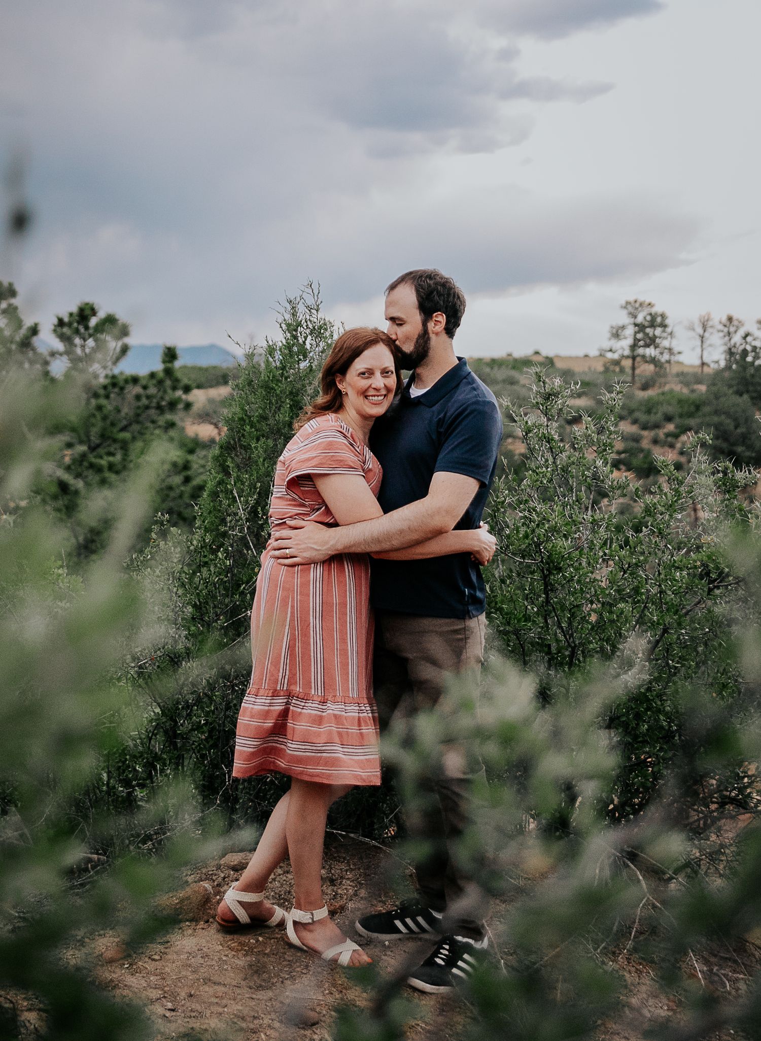A couple shares intimate moments and embraces while posing in a scenic vineyard landscape.