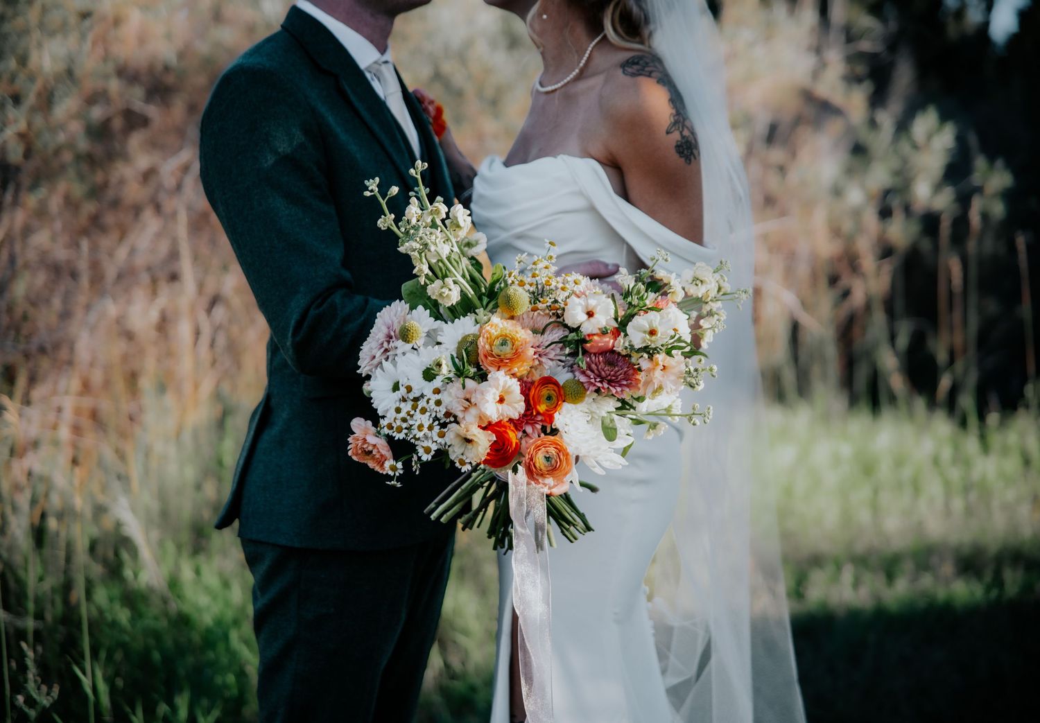 Wedding couple standing in field with autumn foliage and floral bouquet.