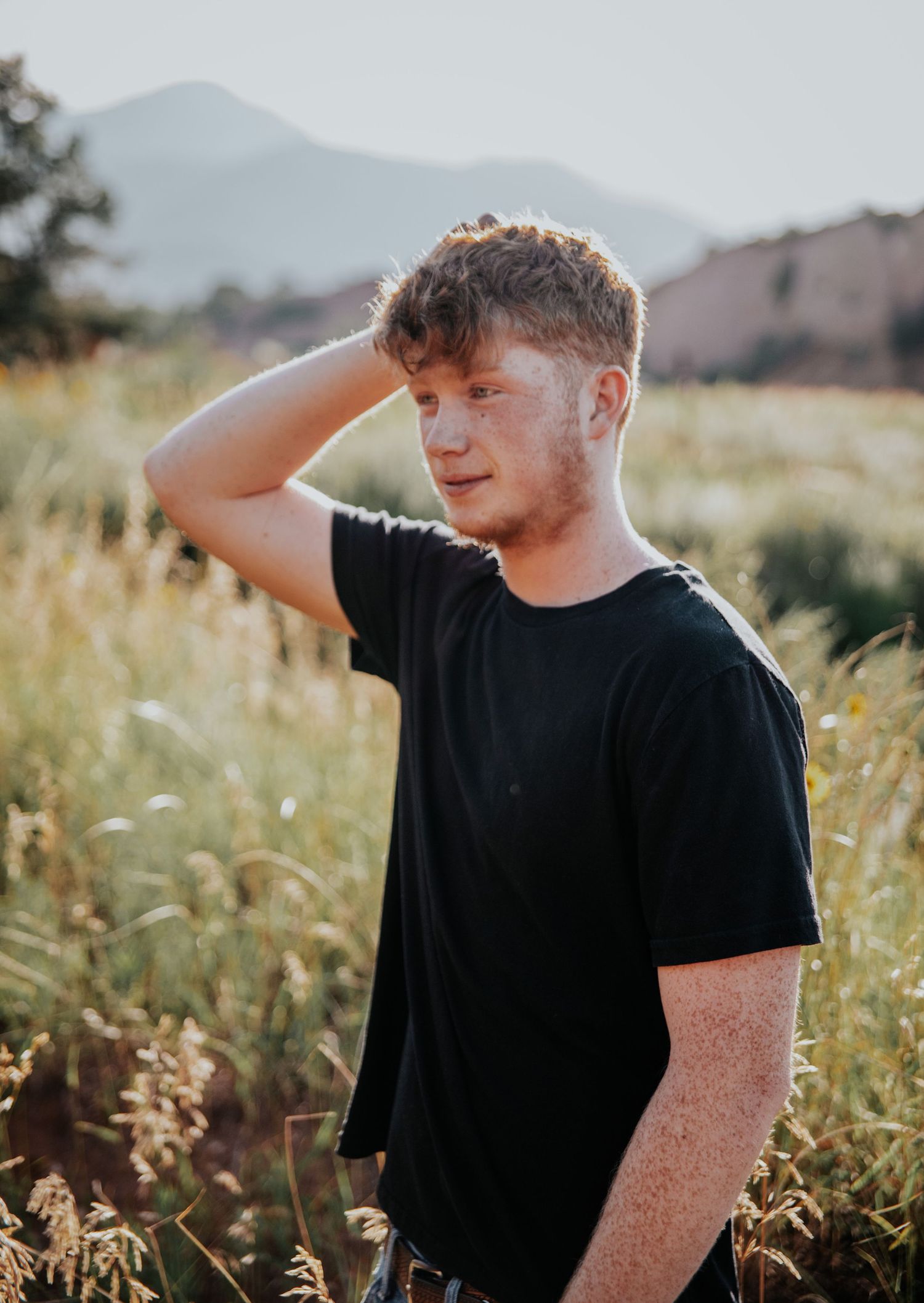 Guy in a grassy field with mountains behind him during senior photo session at Red Rock Open Space in Colorado Springs