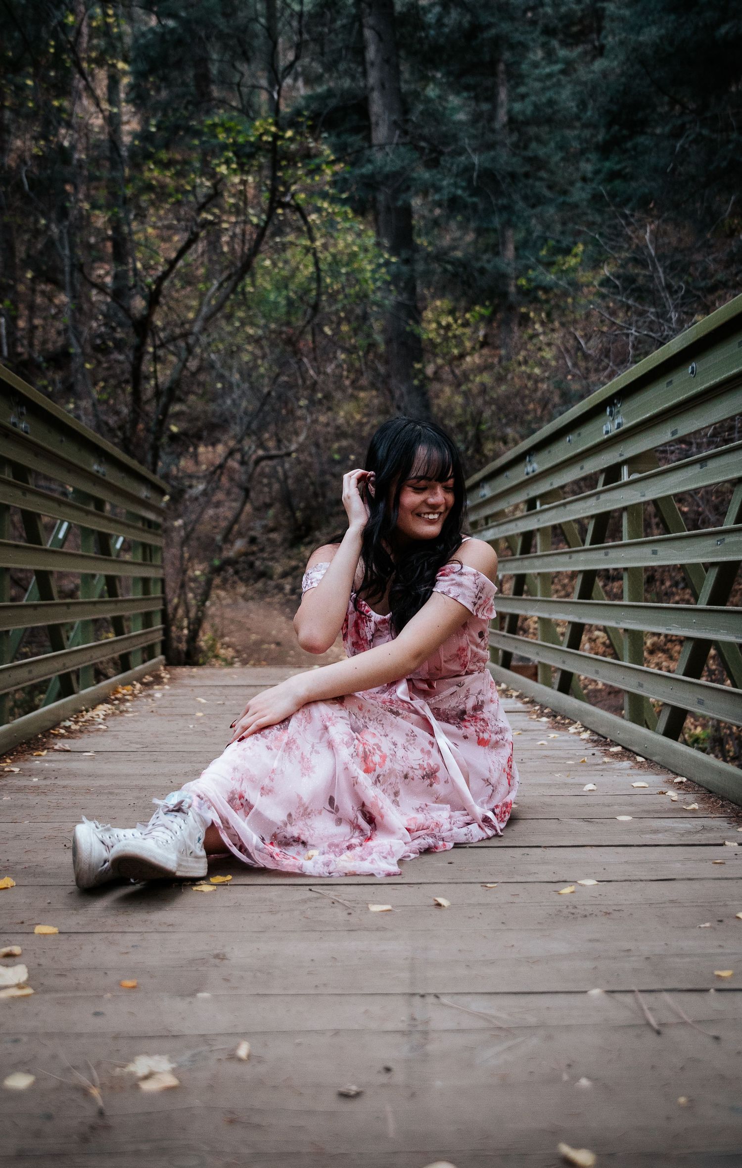 Someone in a romantic pink dress lays gracefully across wooden planks of a scenic bridge.