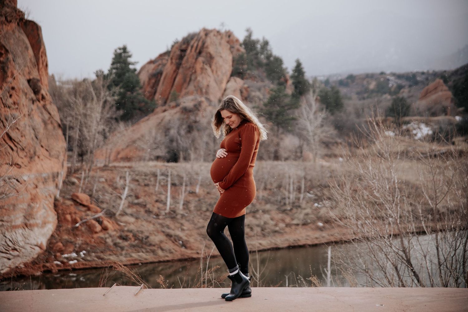 Woman holding pregnant belly in snow at Red Rock Open space during outdoor maternity photo session in Colorado Springs