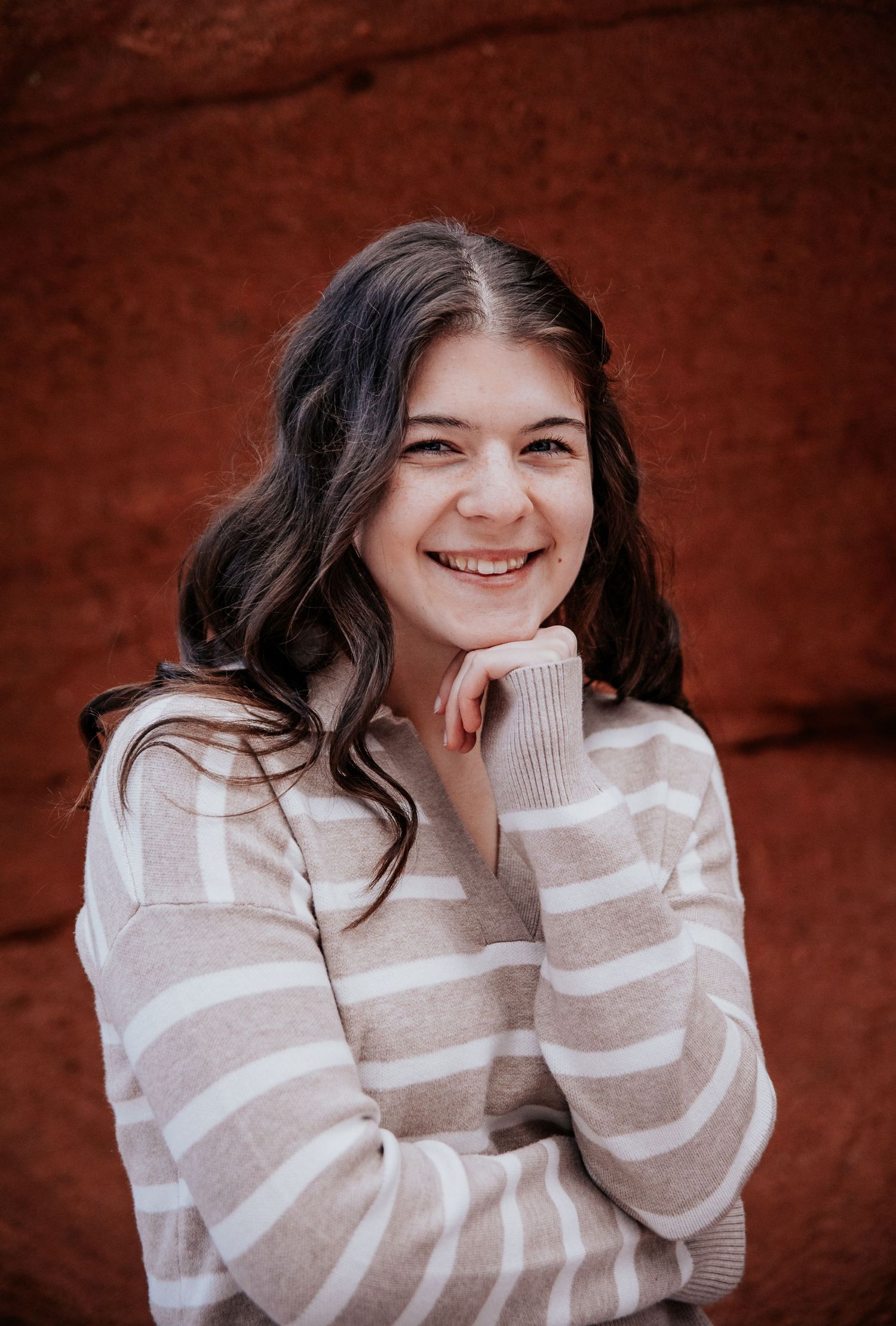 Portrait series against red rock background wearing striped sweater.