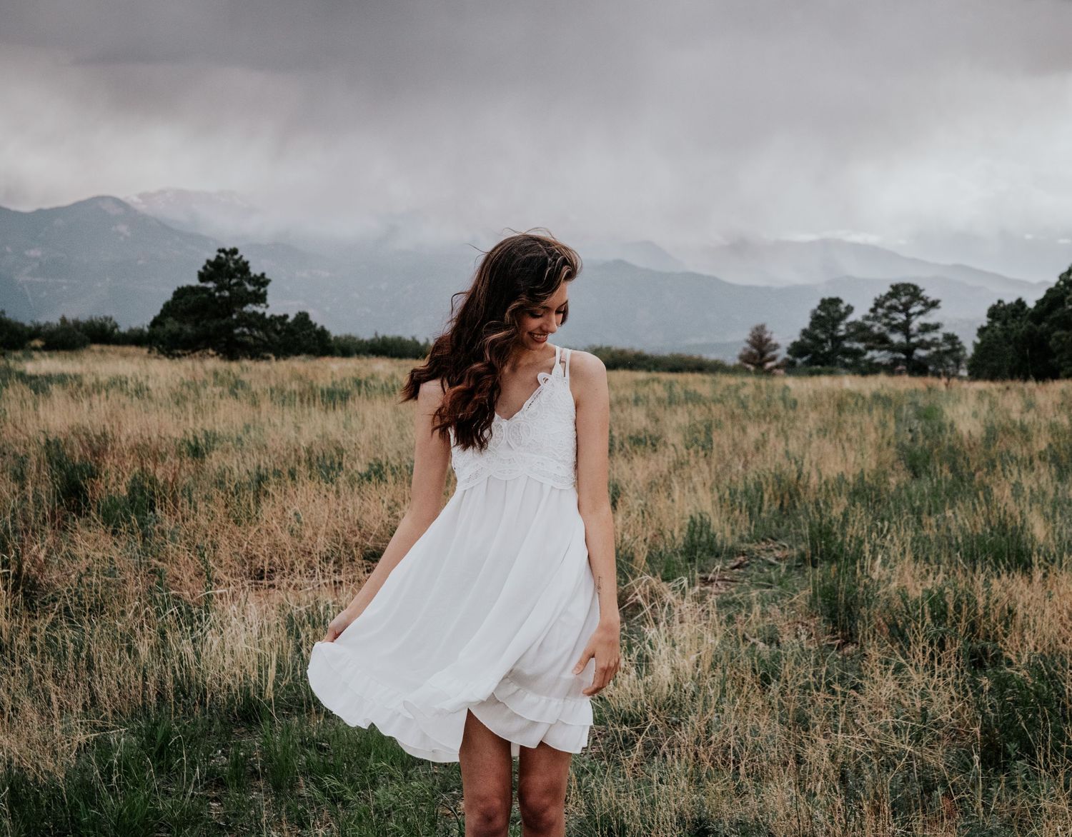 Person wearing white dress walks through golden grass field at sunset.