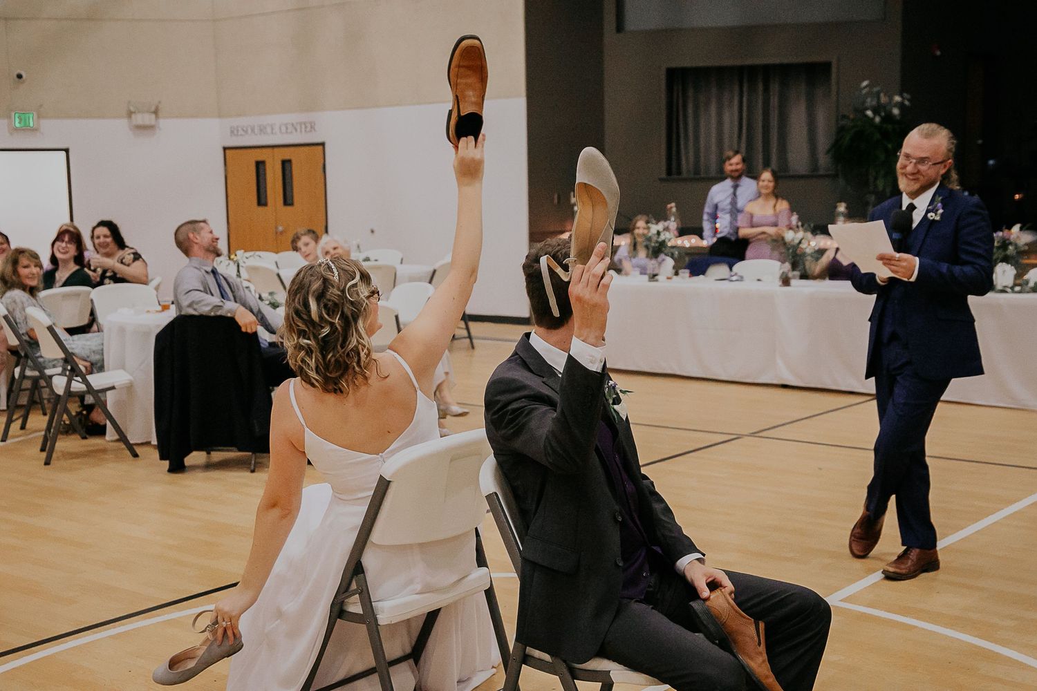 Wedding reception game in a gymnasium with participants holding shoes in the air.